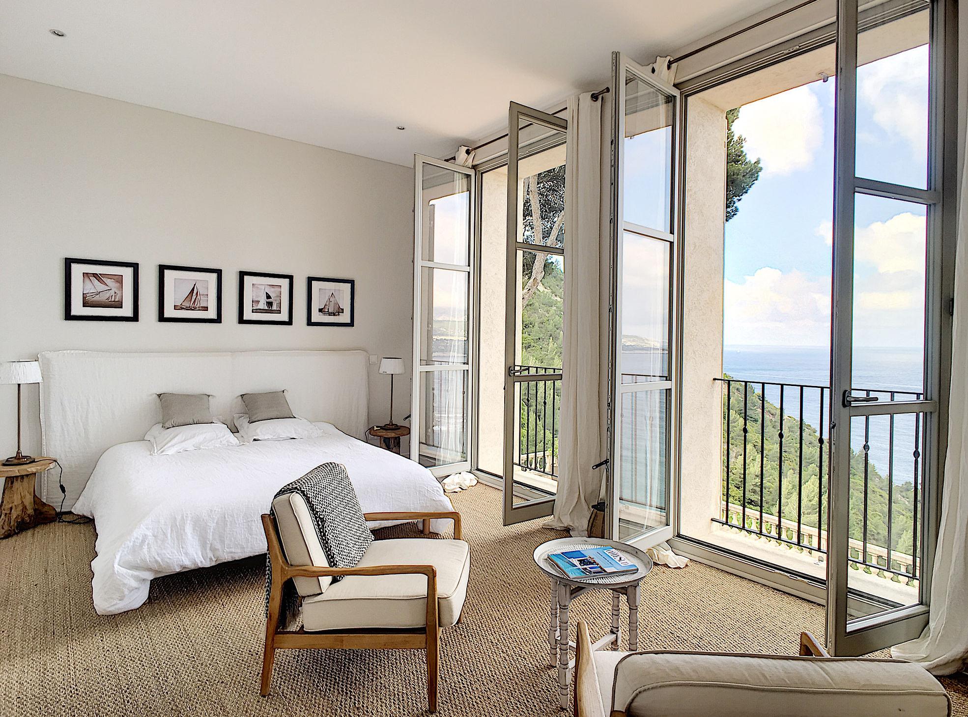 Sunlit bedroom with large glass doors opening to sea-view terrace and natural furnishings