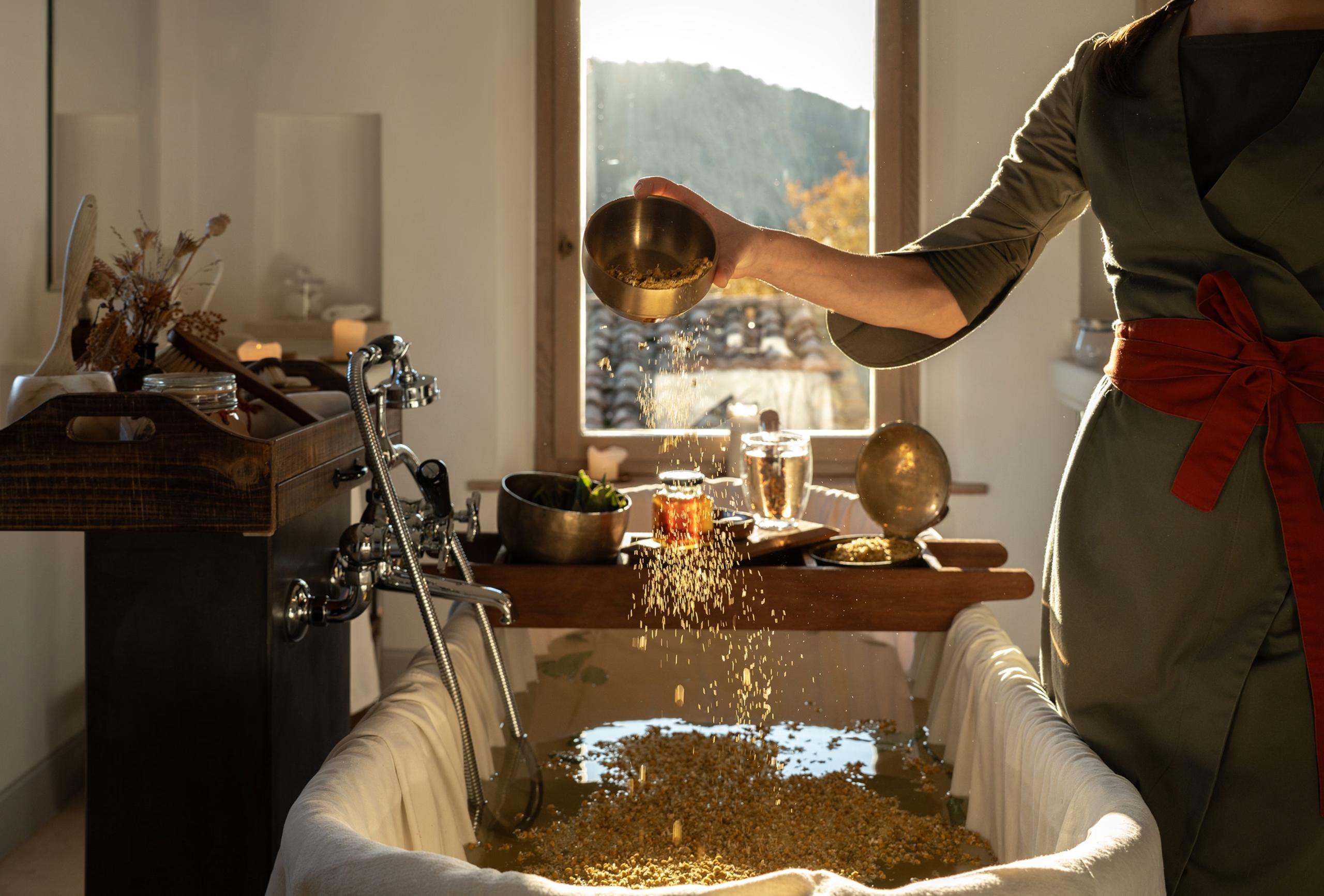 Castello di Reschio: a robed attendant pouring bath salts into a golden vessel beside a window framing distant hills