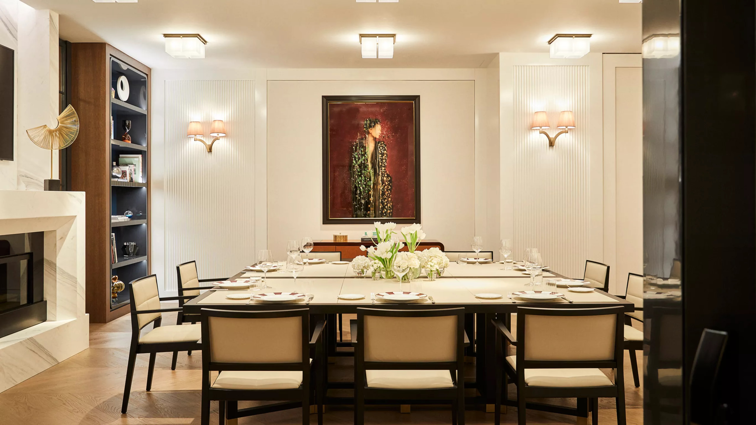 A private dining room with dark wood shelving, cream-colored chairs, and formal table setting