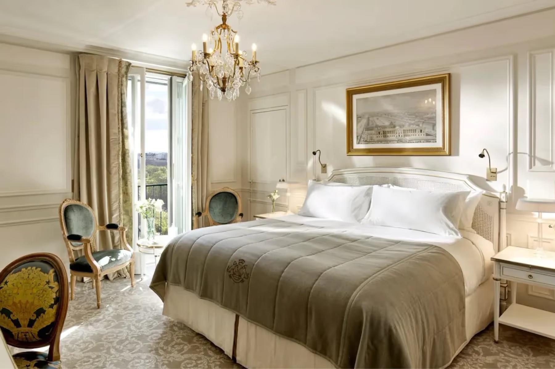A bedroom with bed dressed in neutral linens, framed artwork, and floor-to-ceiling windows