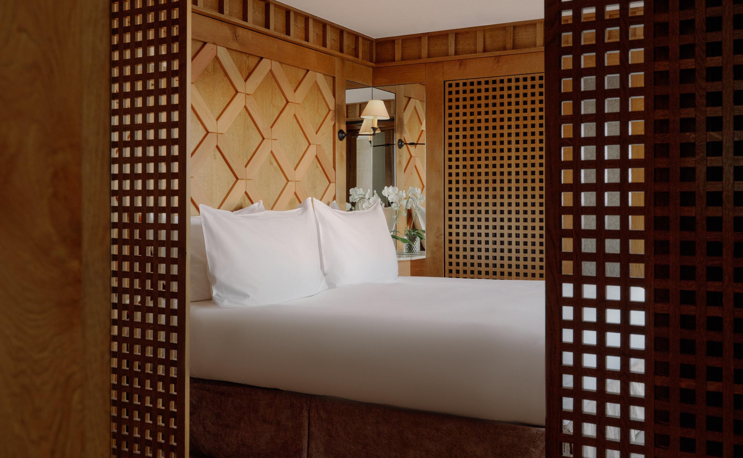Bedroom framed by open wood lattice doors, with a diamond patterned headboard and white bedding