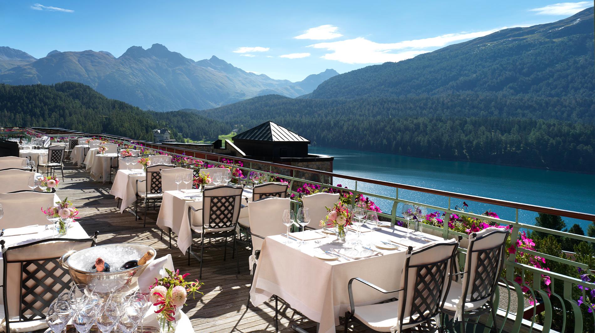 Badrutt’s Palace Hotel: outdoor terrace with white tablecloths overlooking blue lake and snow-capped peaks