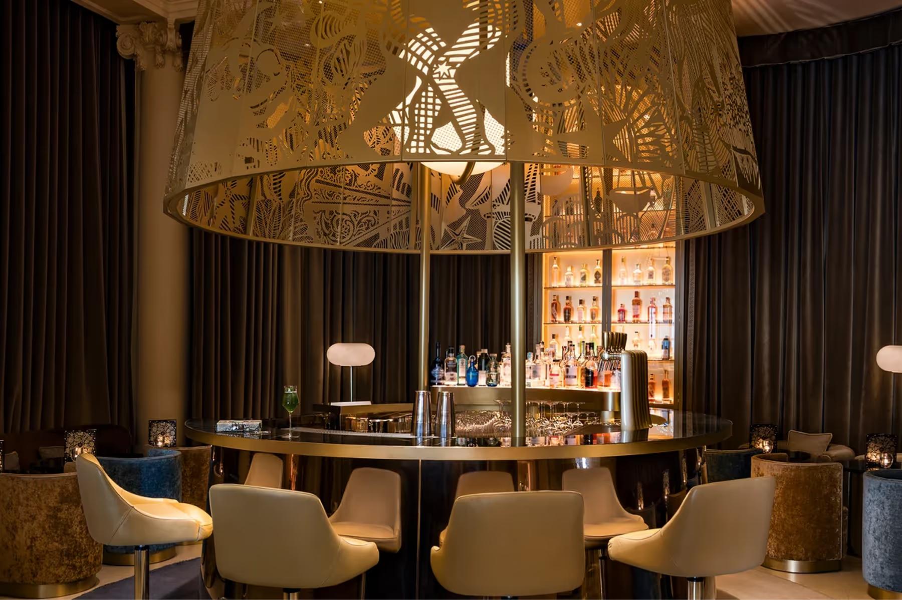 An elegant bar area with gilt accents, cream chairs, and ambient lighting fixtures