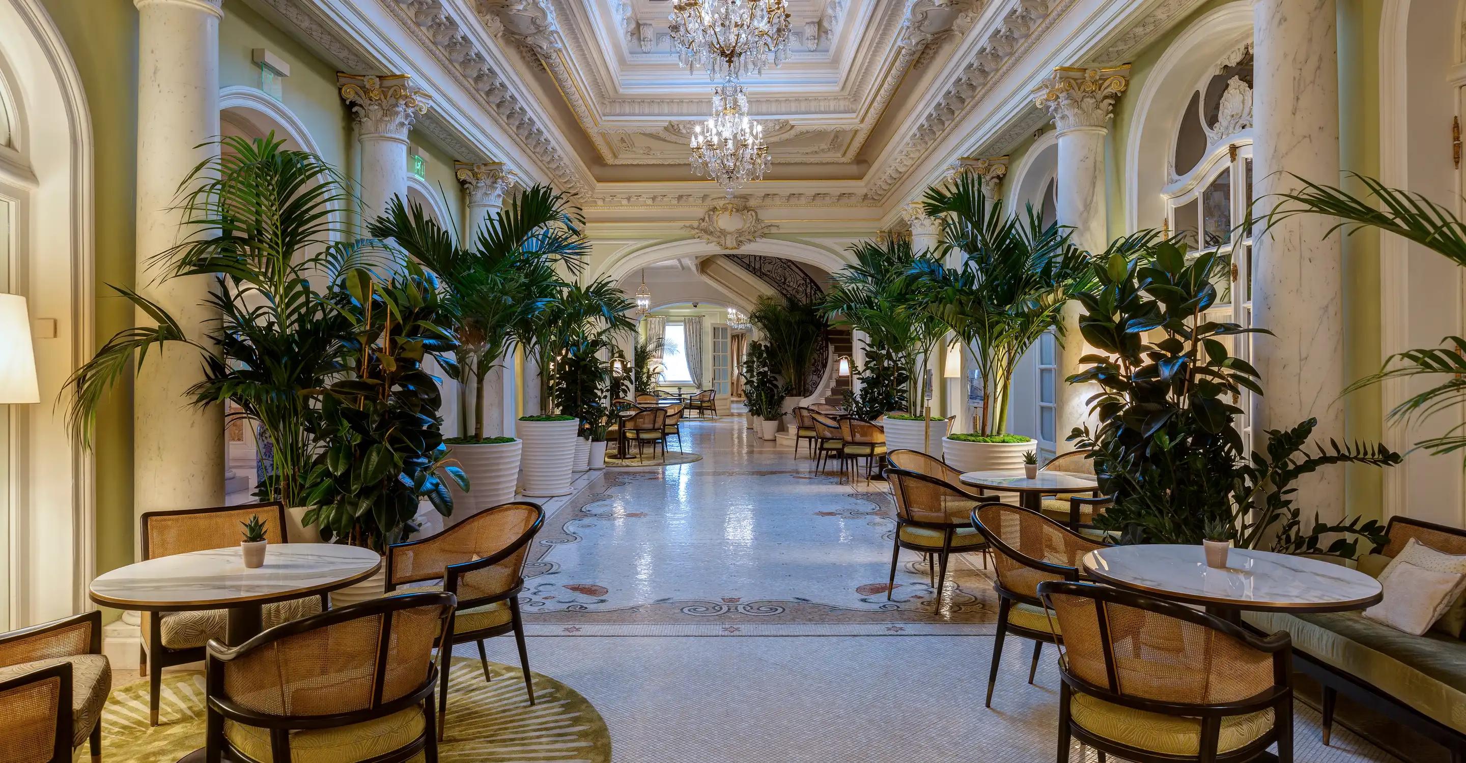 The Belle Époque atrium with coffered ceiling and crystal chandelier, palm trees, and marble floors