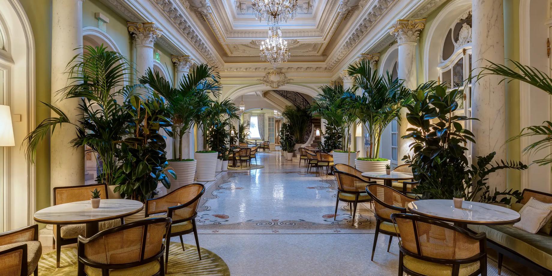 The Belle Époque atrium with coffered ceiling and crystal chandelier, palm trees, and marble floors