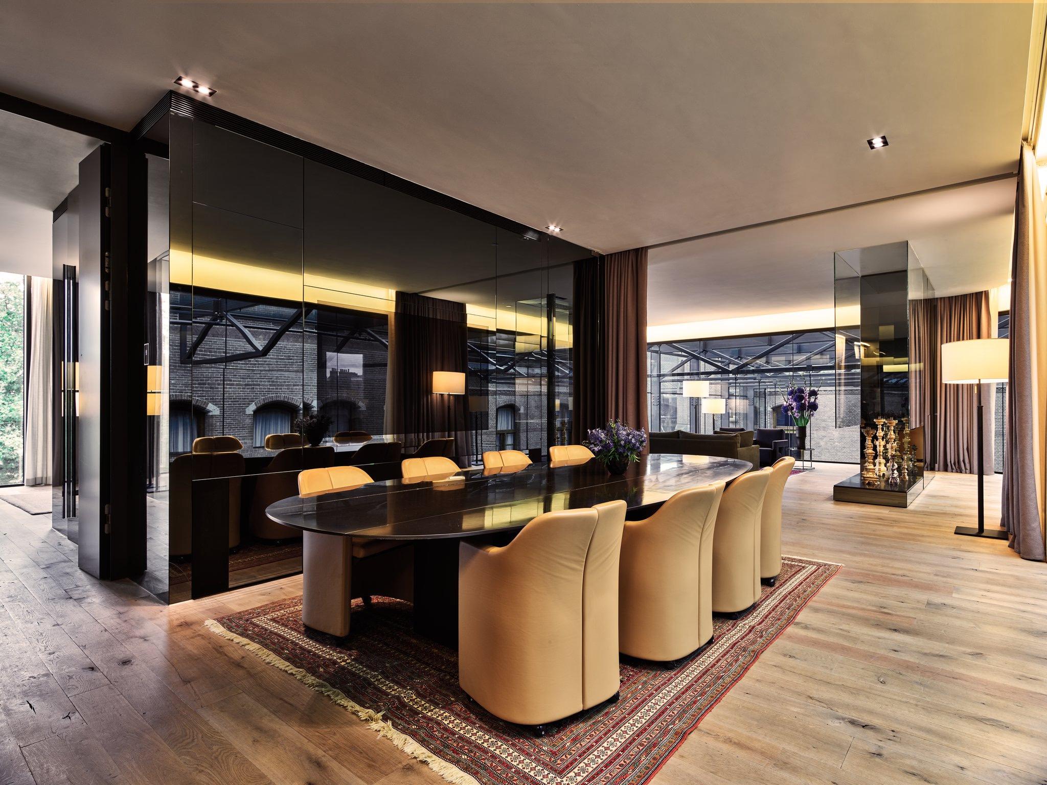 Mandarin Oriental Conservatorium, Amsterdam: dining room with an oval table and cream chairs on a red patterned rug, beside a dark glass wall