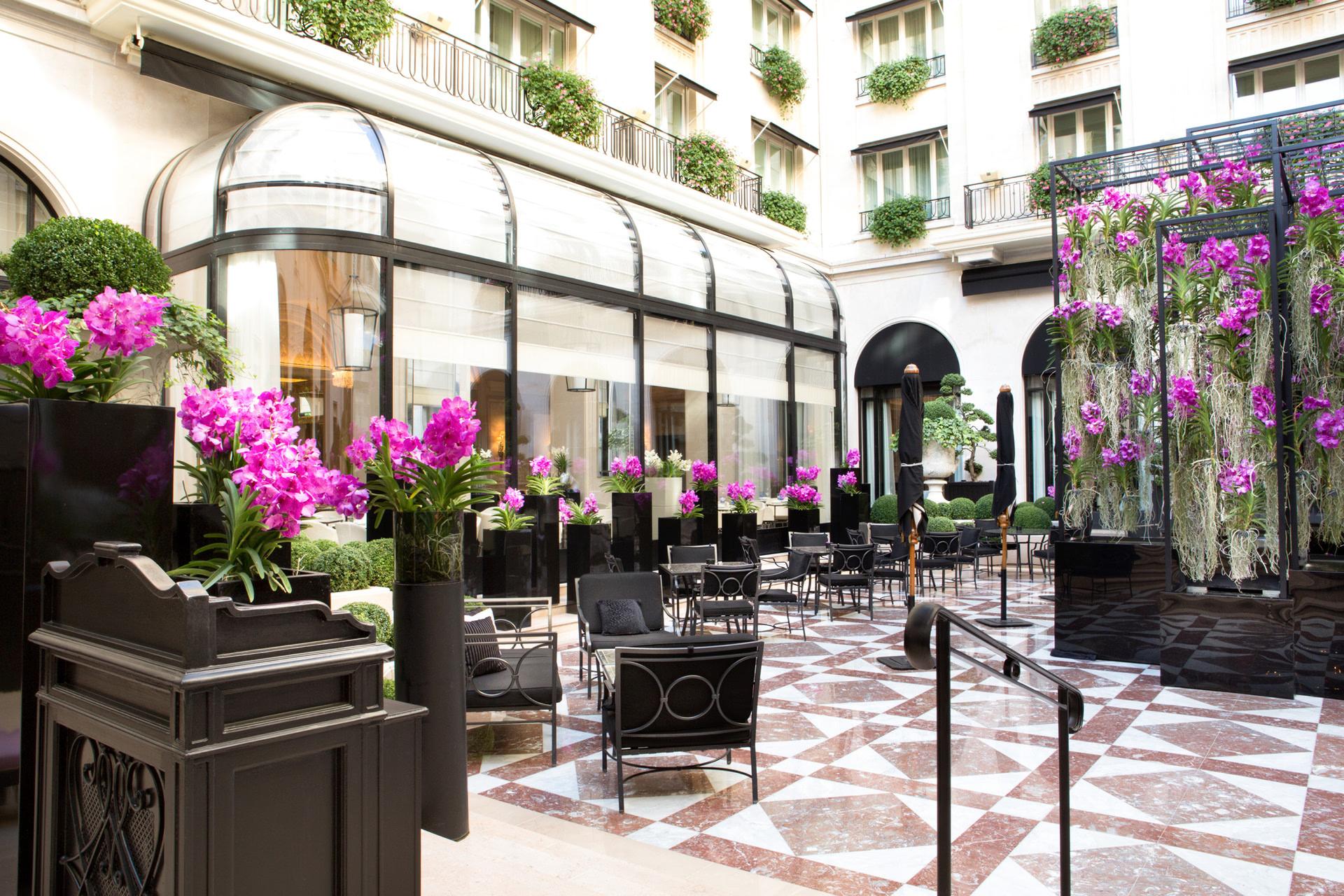 Four Seasons Hotel George V: a formal courtyard with magenta flowers, black metal chairs, and a geometric marble floor beneath white classical facades