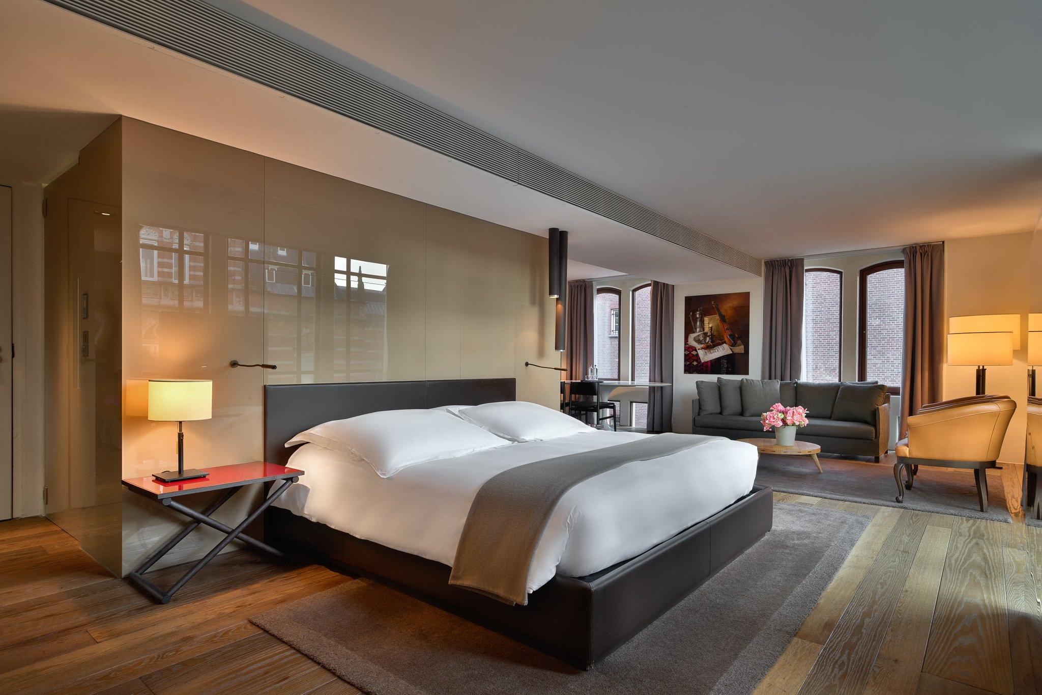 Mandarin Oriental Conservatorium, Amsterdam: spacious suite with dark wood bed frame, cream linens, window seating area, and warm lighting