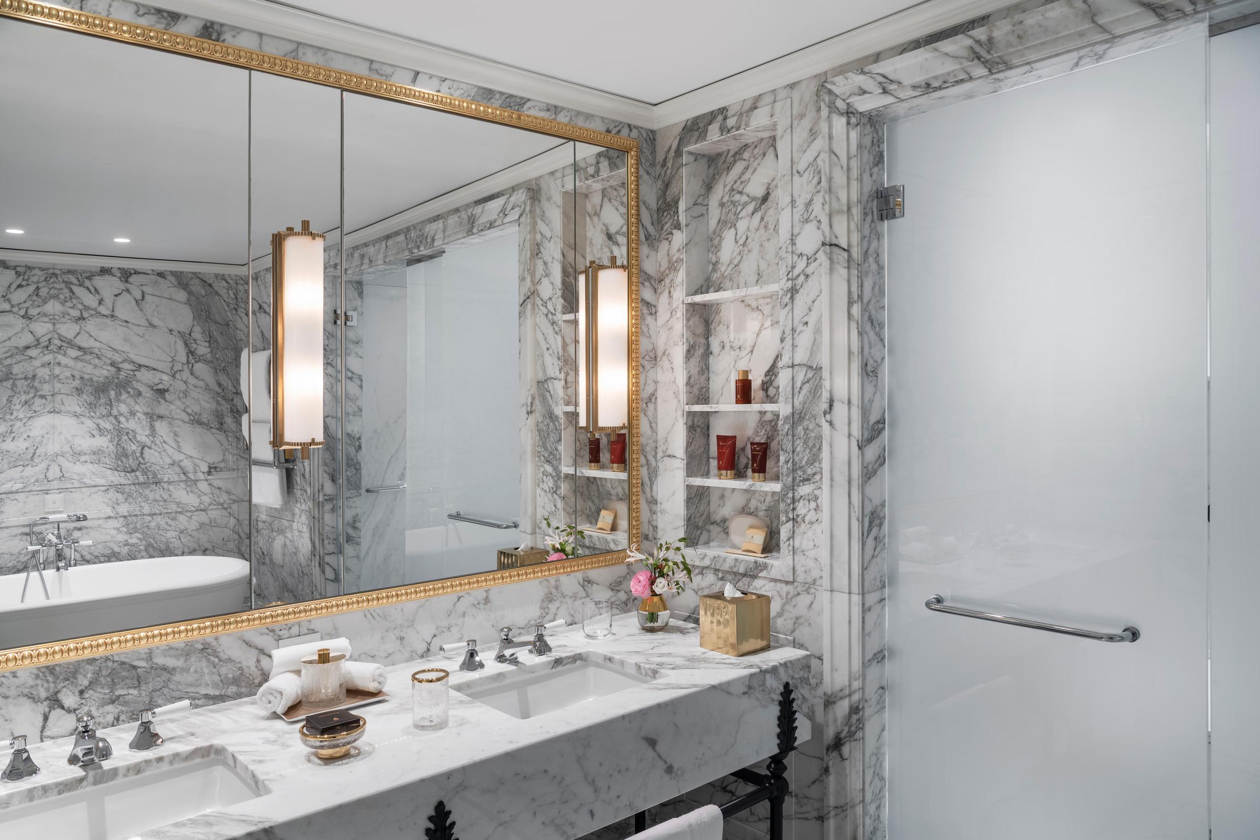 Badrutt’s Palace Hotel: marble bathroom with brass fixtures, white sink, and framed mirror