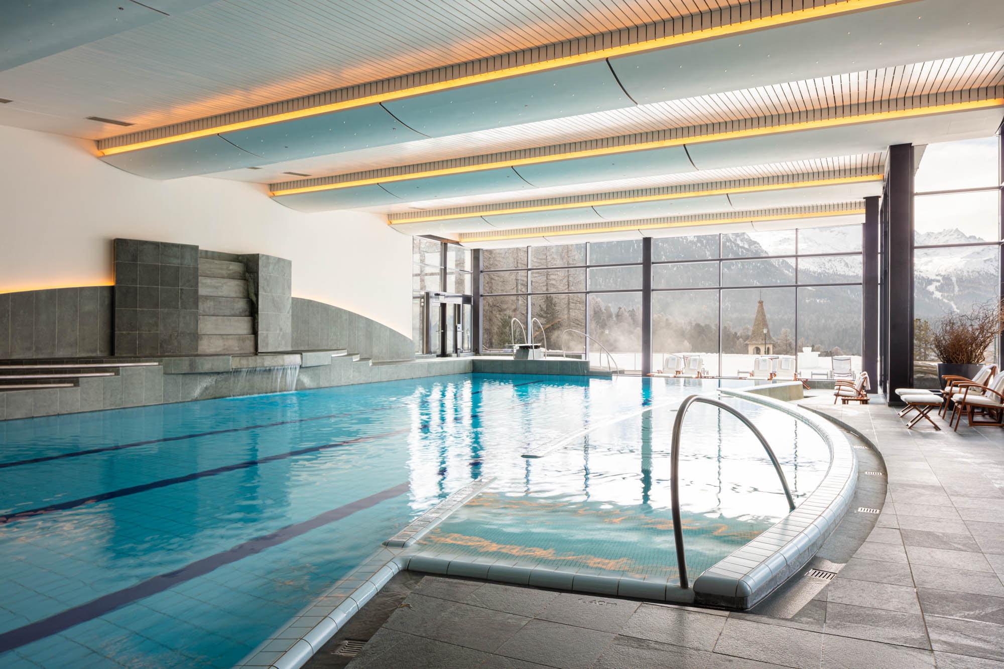 Suvretta House: an indoor lap pool with large windows, integrated hot tub, and orange accent lighting