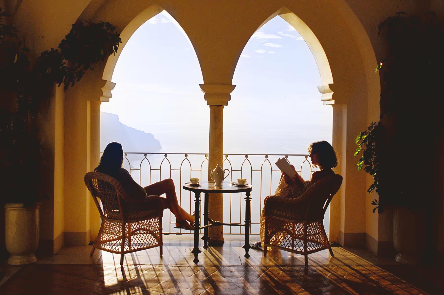 Silhouetted couple seated under Moorish columns with panoramic sea vista at sunset