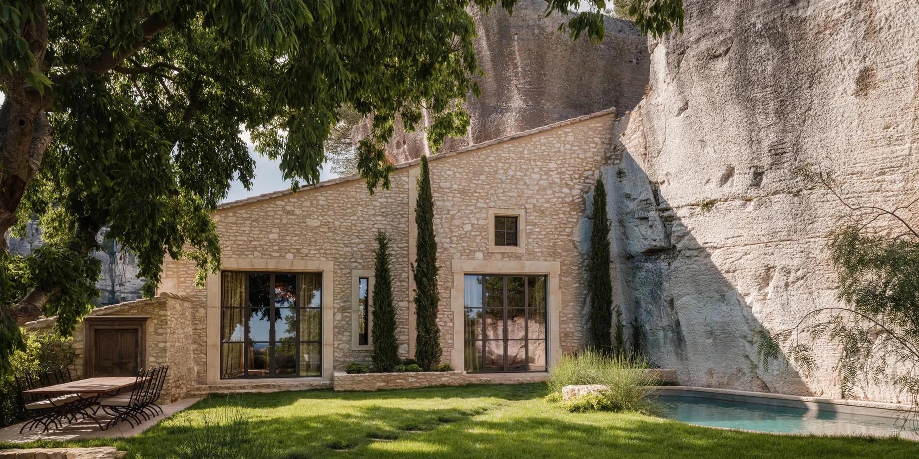 Stone villa with modern glass doors, wooden pergola, grass courtyard, pale turquoise pool, limestone cliff backdrop