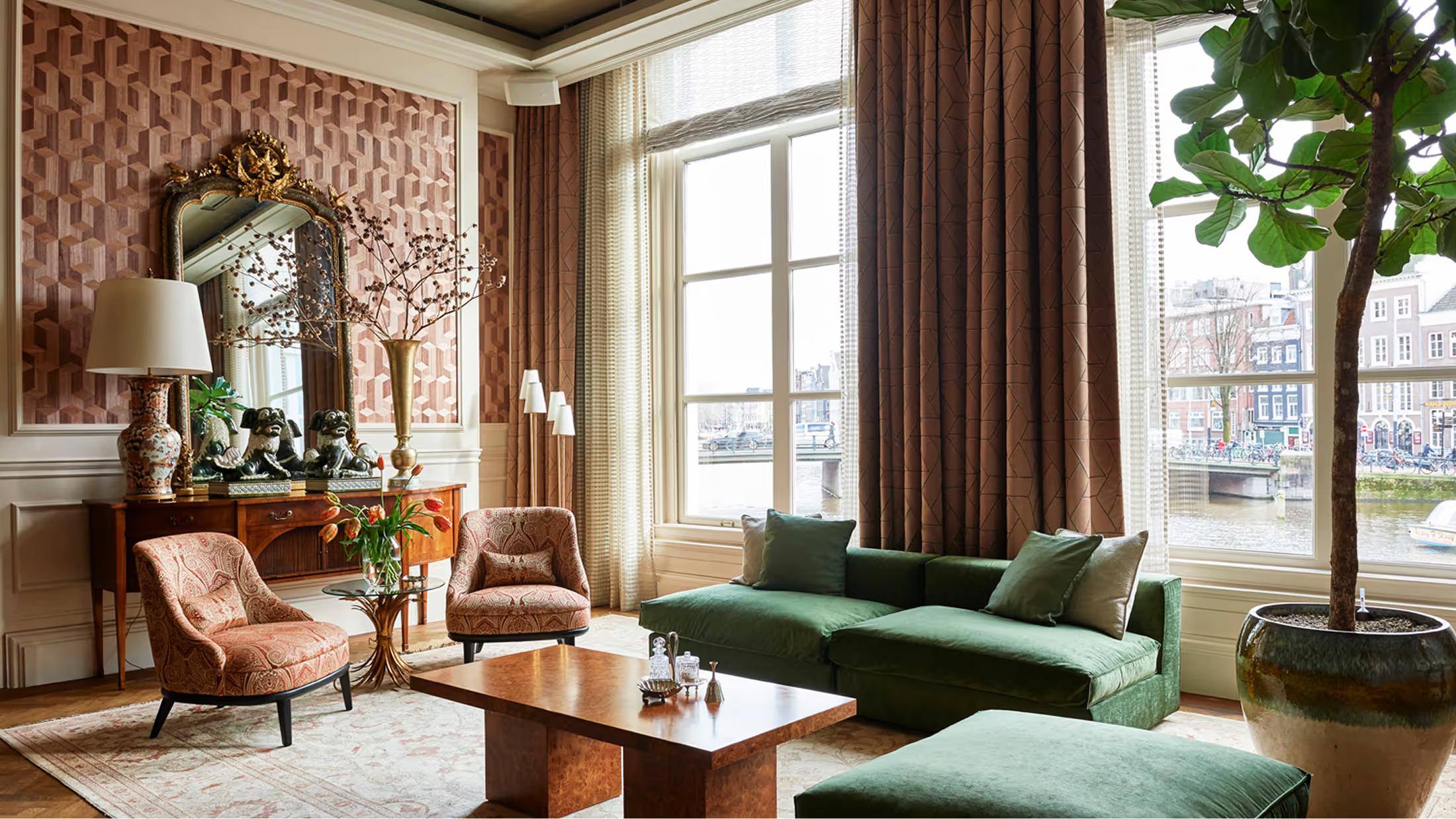 Lobby lounge with green sofa, fireplace, and arched windows overlooking the Amstel