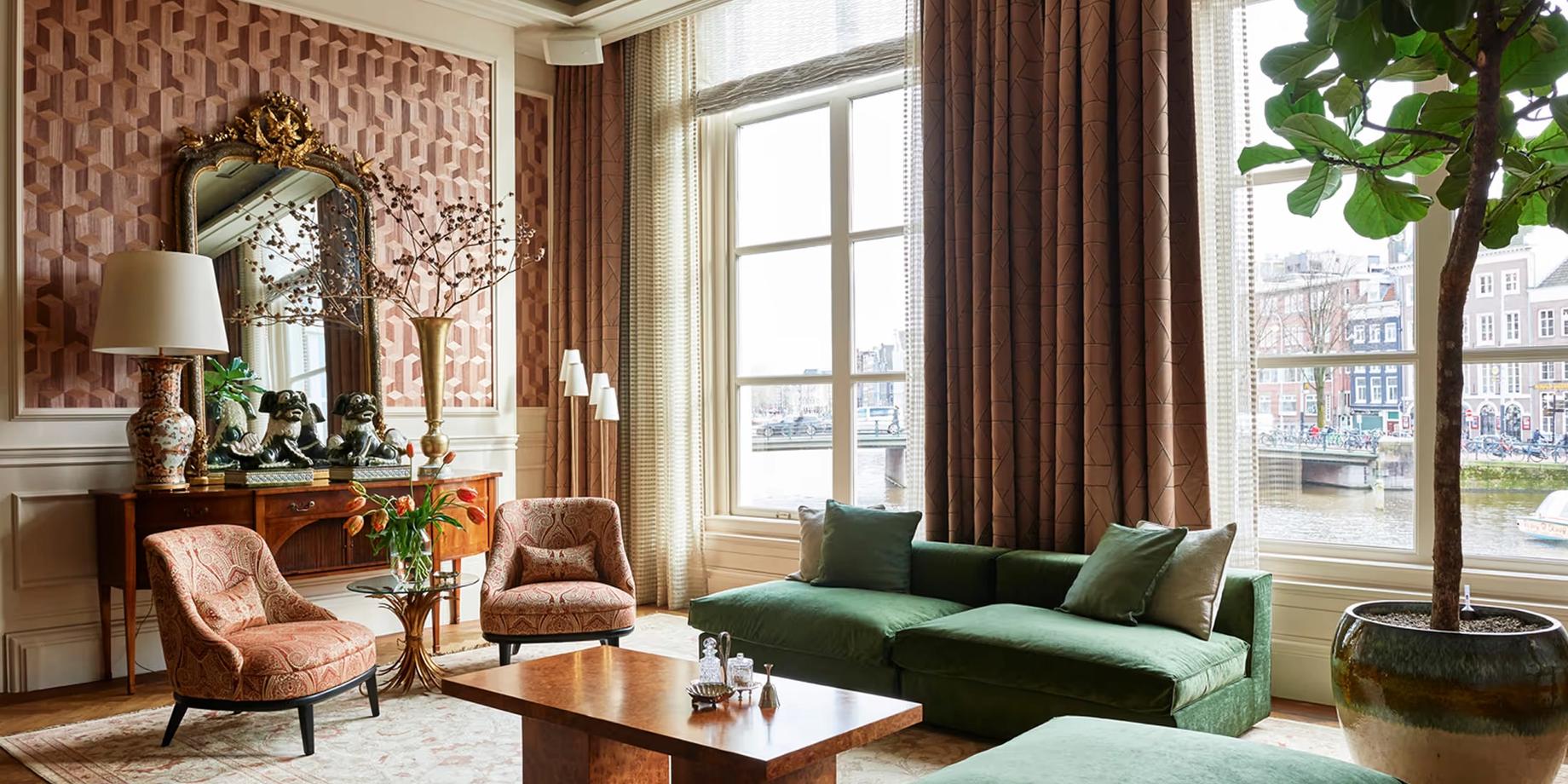 Lobby lounge with green sofa, fireplace, and arched windows overlooking the Amstel