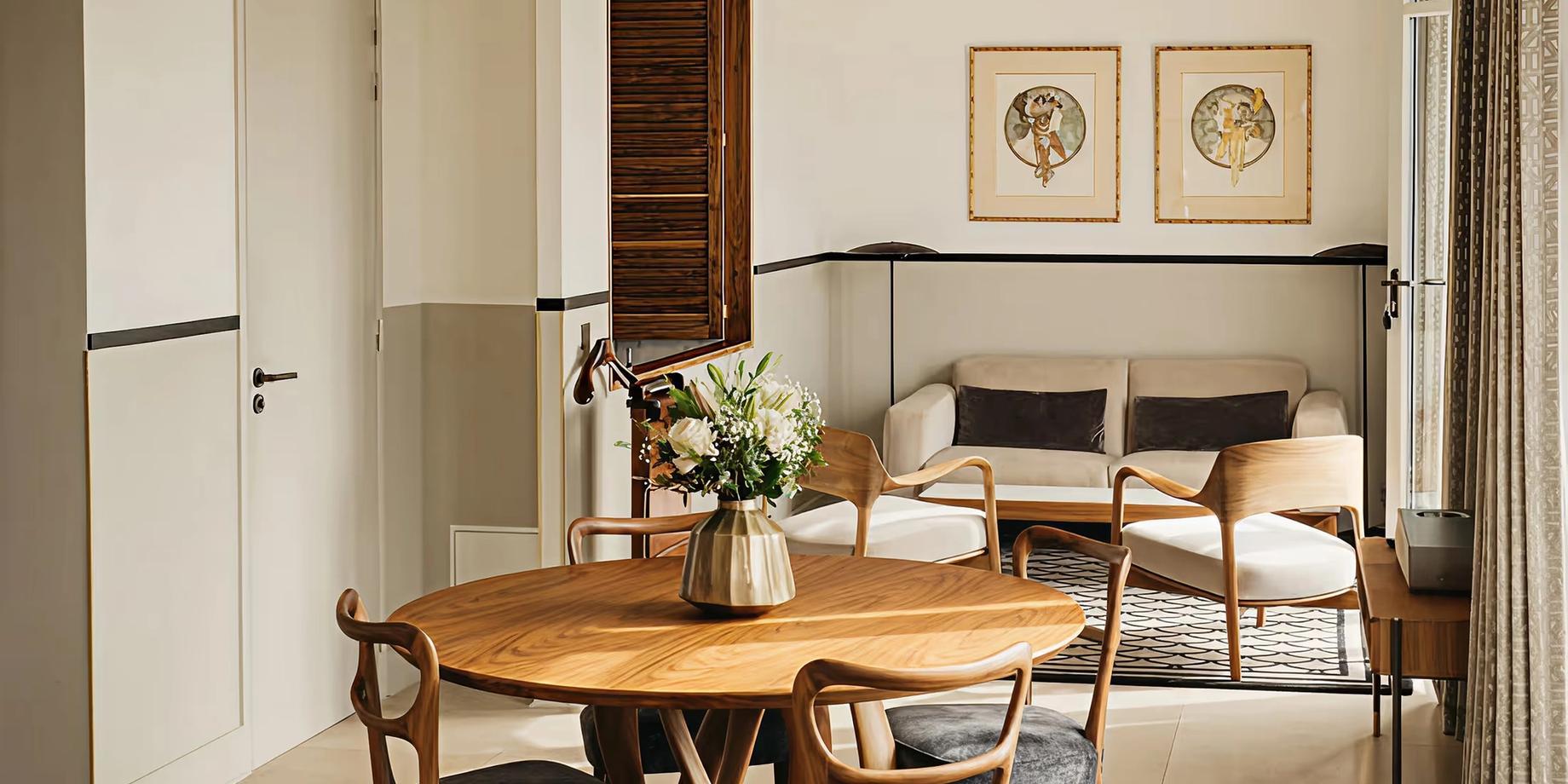 A minimalist dining room with wood table, woven chairs, and framed botanical prints