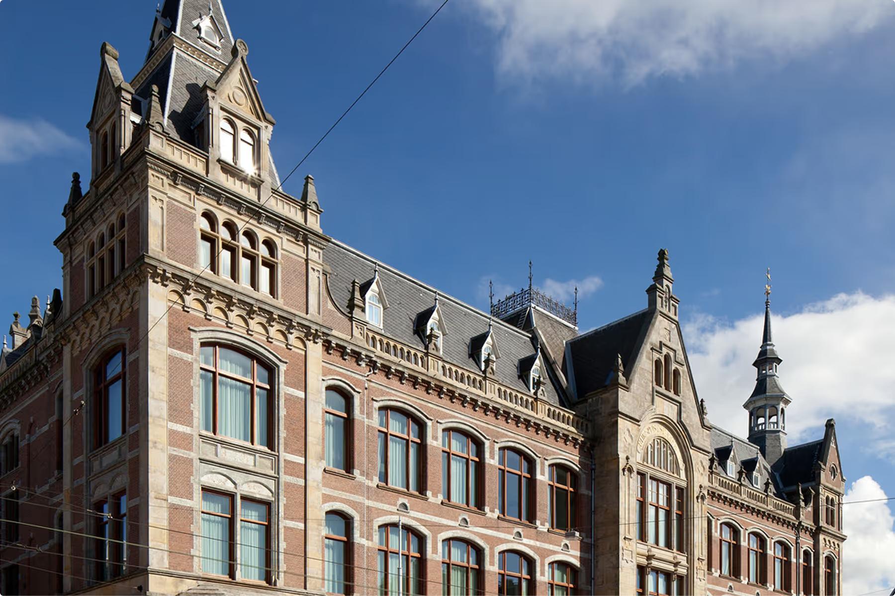 Mandarin Oriental Conservatorium, Amsterdam: brick-and-stone facade of the 19th-century building, with towers, dormers, and tall arched windows under a blue sky