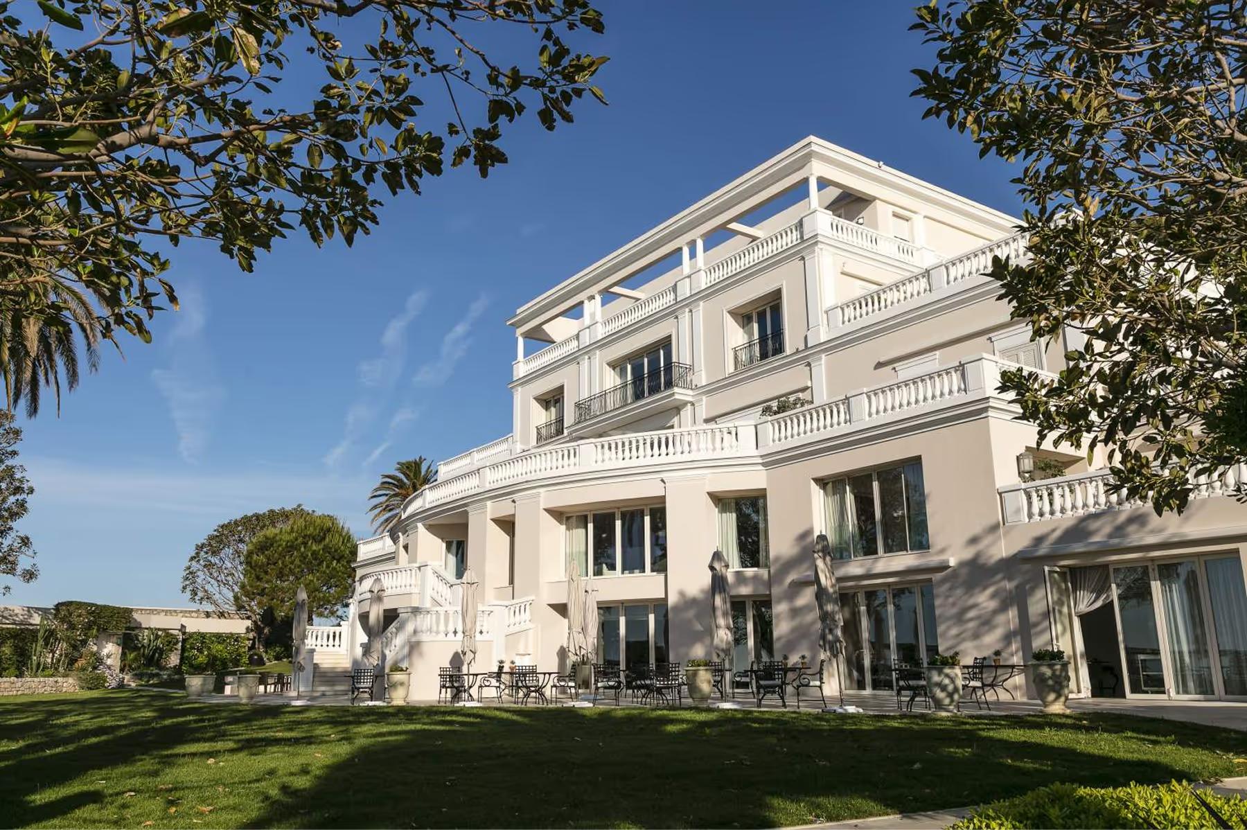 A neoclassical white villa with balconies overlooking manicured gardens