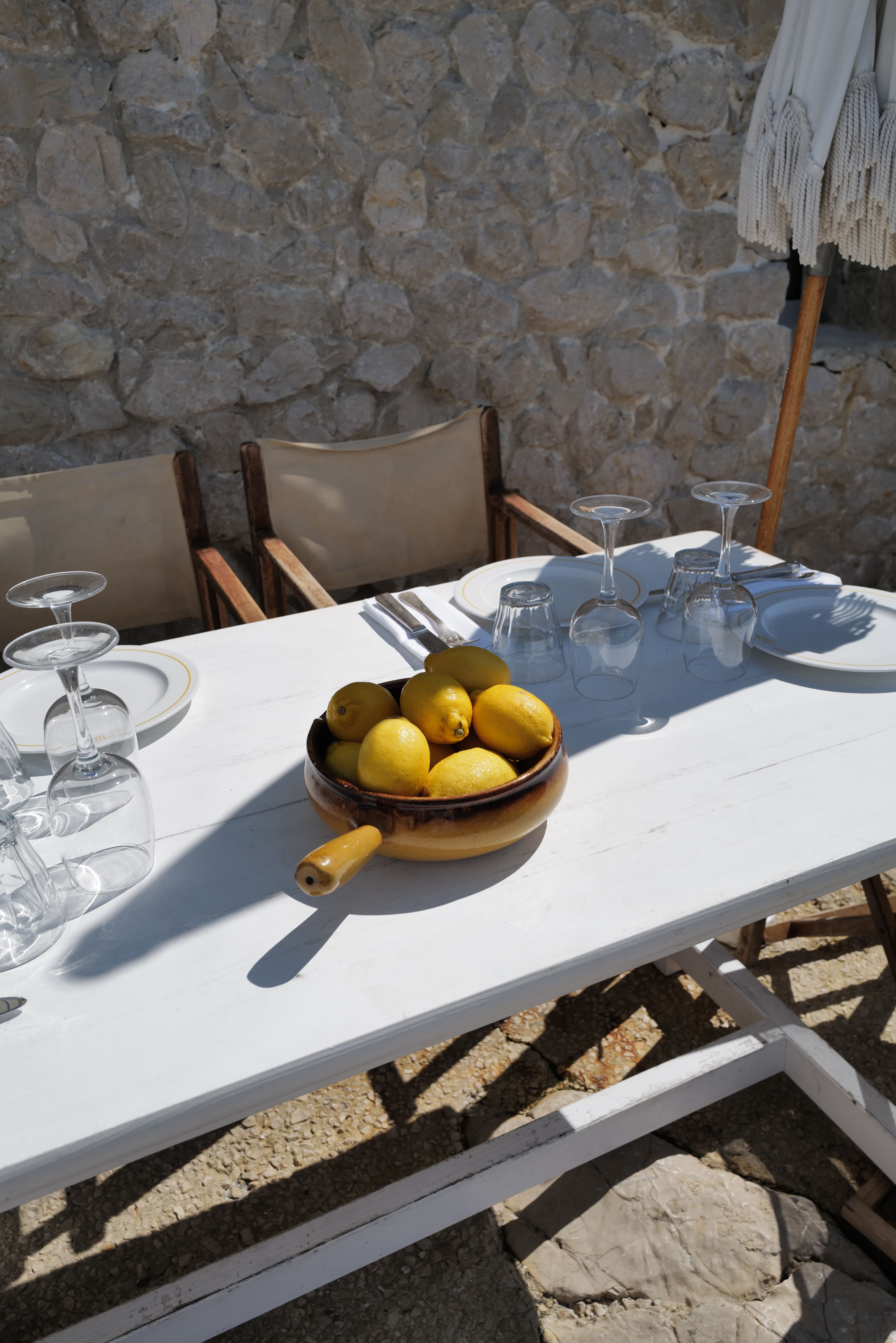 A bowl of lemons on a white table set for lunch against a dry stone wall