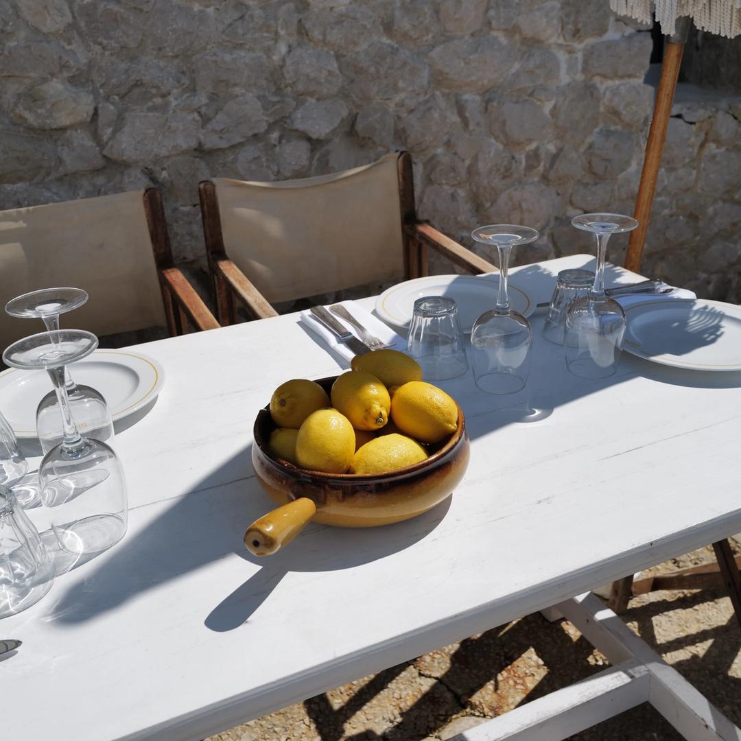 A bowl of lemons on a white table set for lunch against a dry stone wall