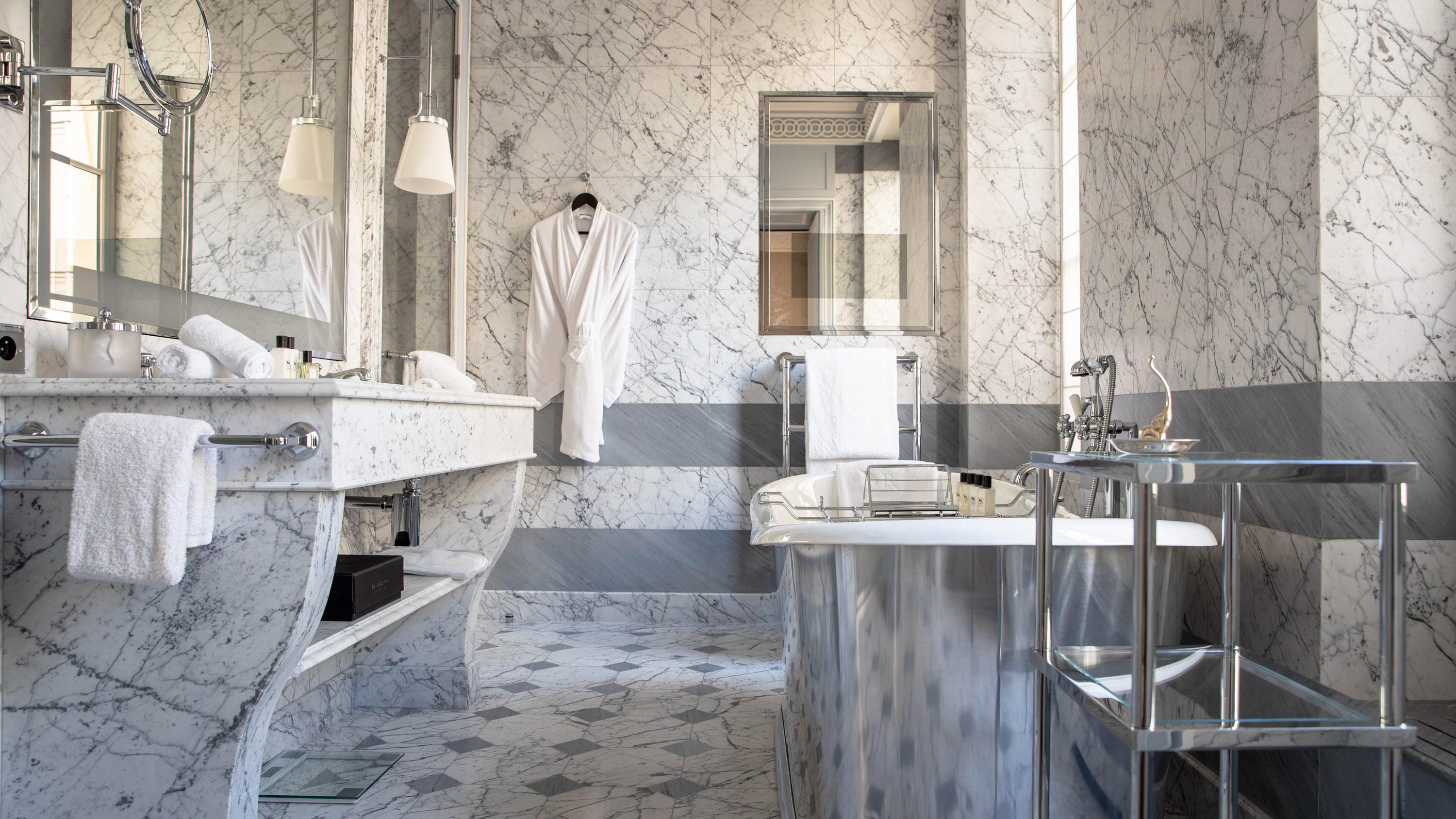 A marble bathroom with white and gray tones, featuring brass fixtures and a stone sink