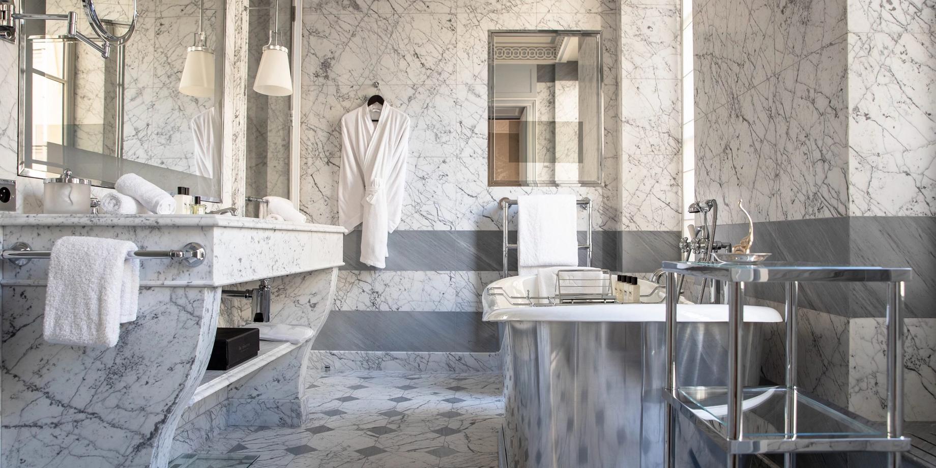 A marble bathroom with white and gray tones, featuring brass fixtures and a stone sink