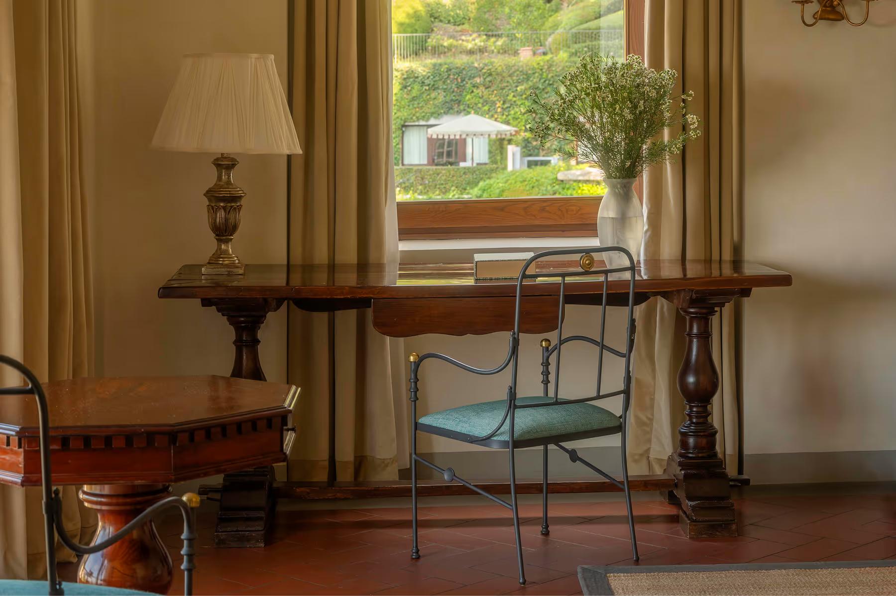 A study nook with wooden desk, green velvet chair, and view to gardens and grounds