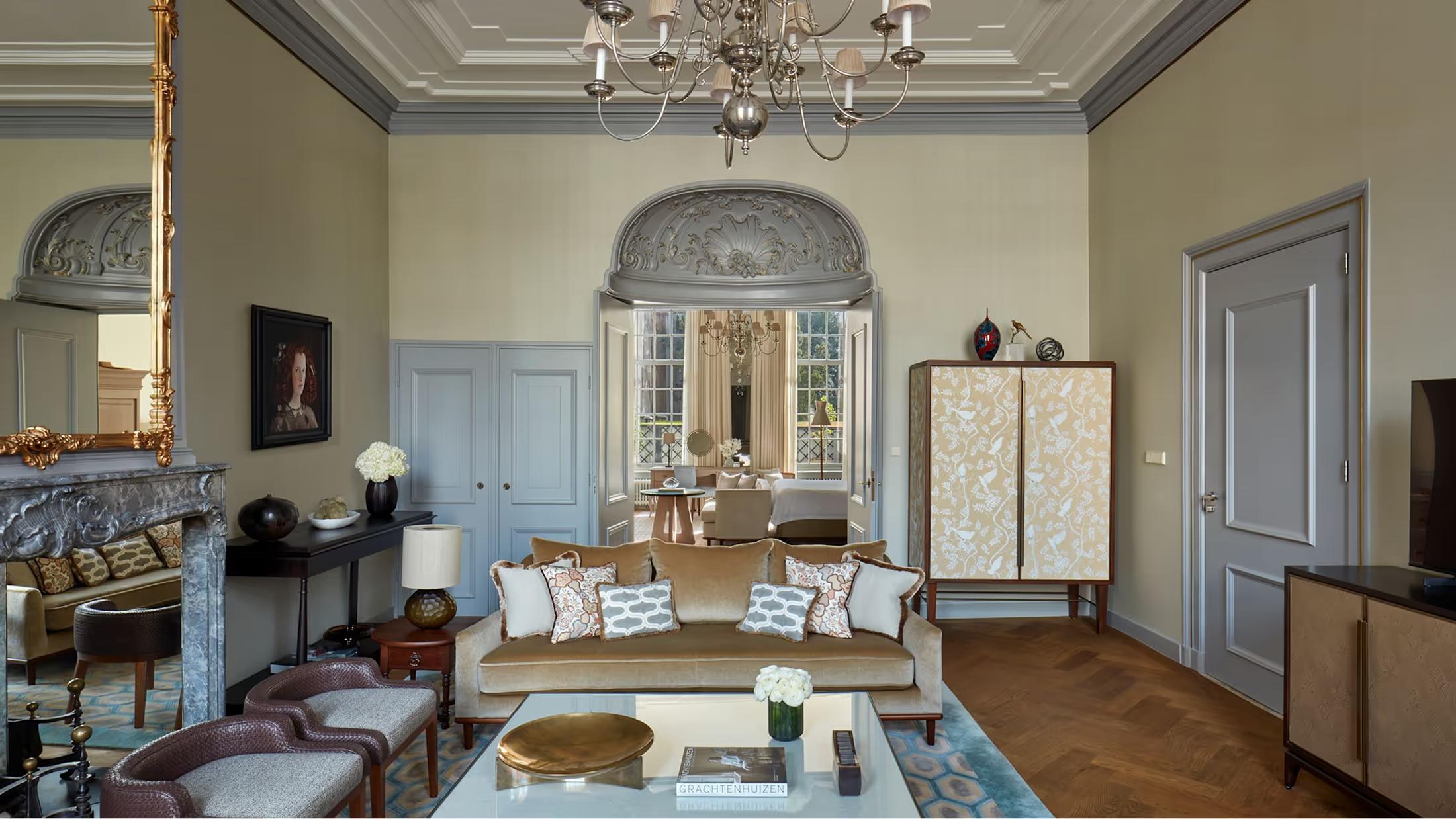 A formal sitting room with high ceilings and ornamental moldings, furnished with period pieces and a blue-cushioned sofa near tall windows