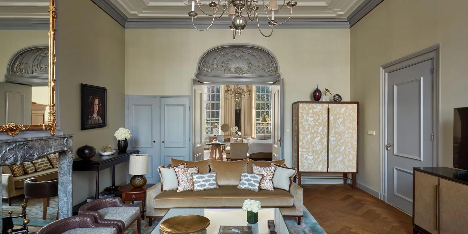 A formal sitting room with high ceilings and ornamental moldings, furnished with period pieces and a blue-cushioned sofa near tall windows