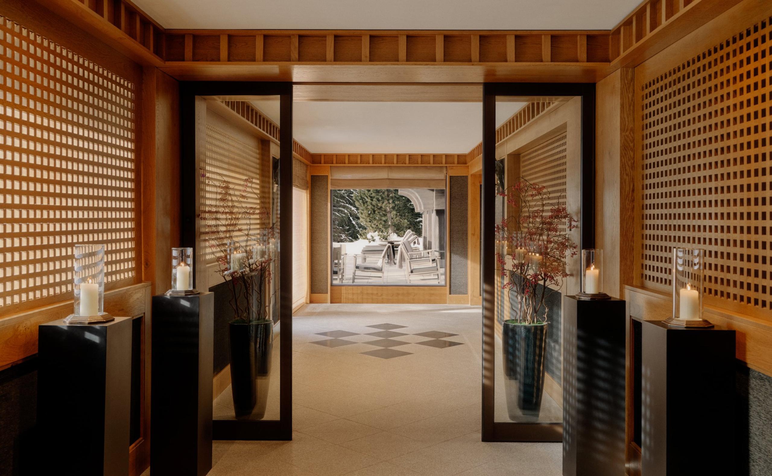 Entry corridor with mirrored screens, candlelit pedestals, and a checkerboard floor leading outside