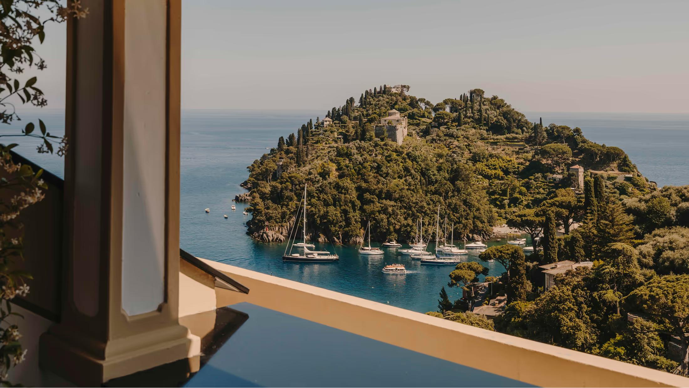 A terraced balcony with wood railings framing the Ligurian Sea and forested harbor