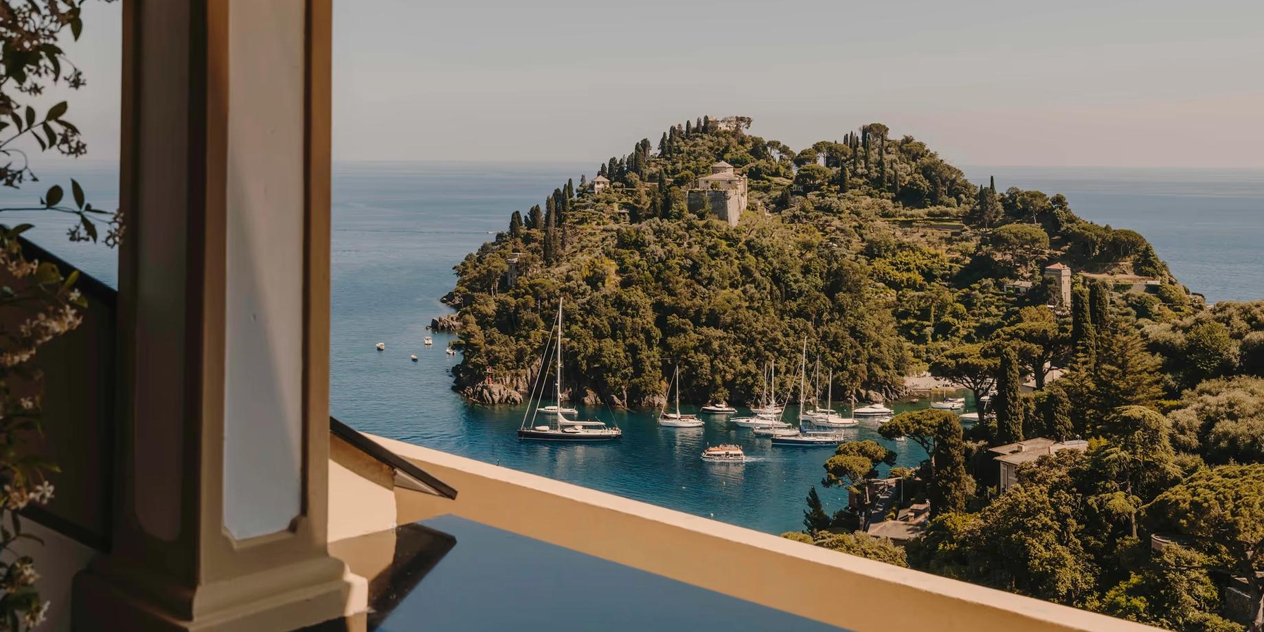 A terraced balcony with wood railings framing the Ligurian Sea and forested harbor
