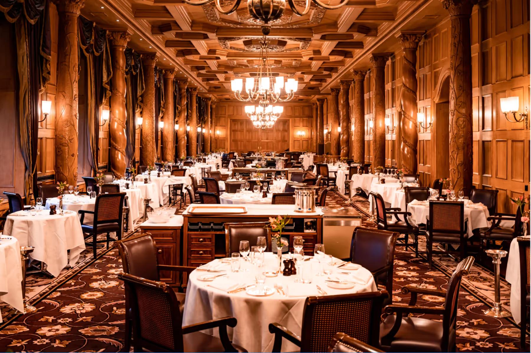 Suvretta House: a grand dining hall with ornate golden ceiling, crystal chandeliers, and formally set white-draped tables