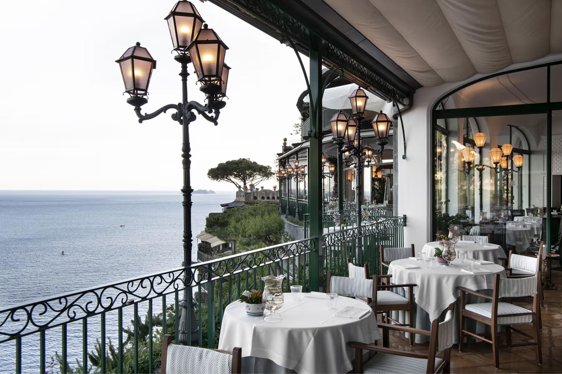 Il San Pietro di Positano: elegant covered patio dining with white tablecloths, brass lanterns, railing, and sea views