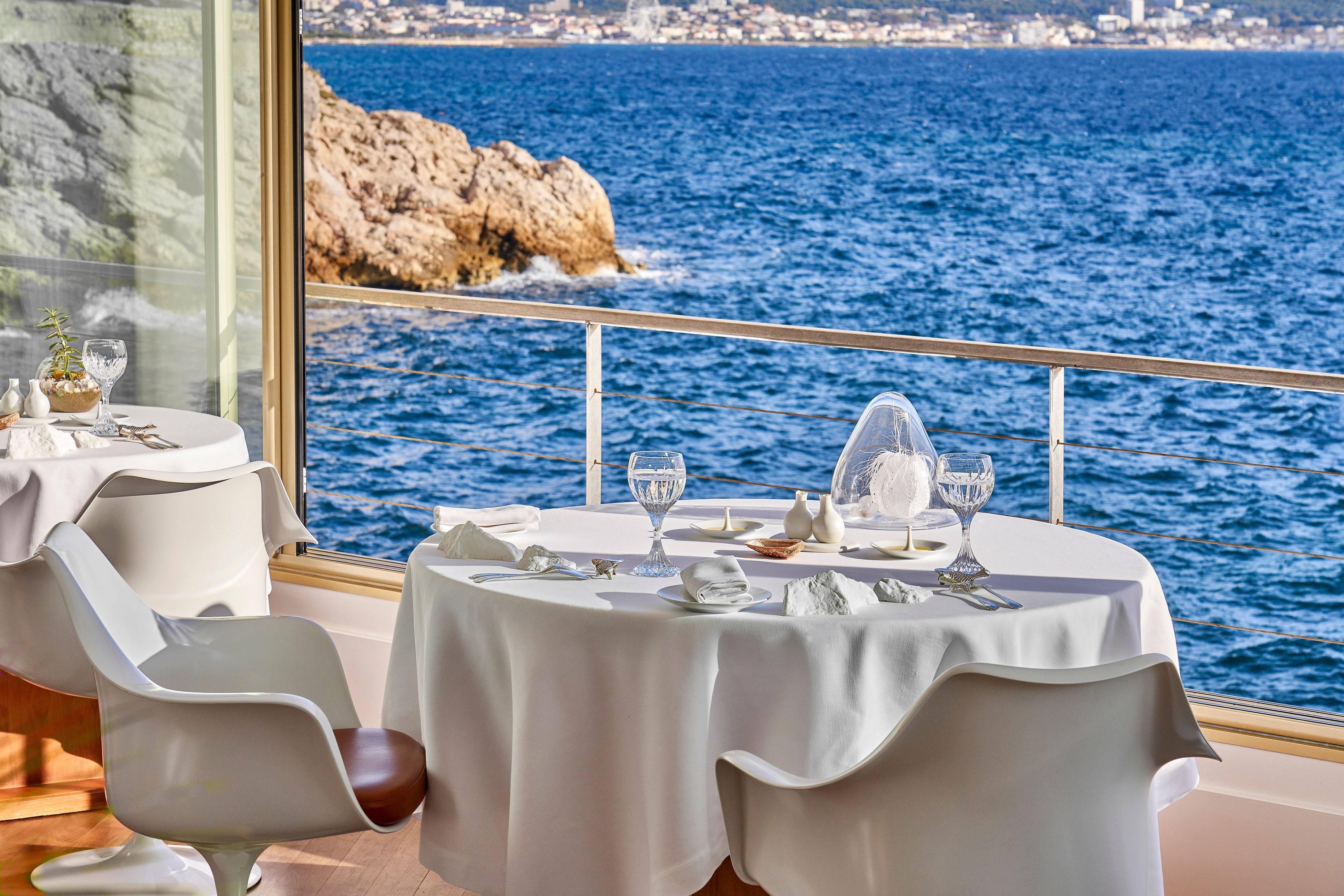 A table laid in white by the window at Le Petit Nice, the rocks and the open sea below