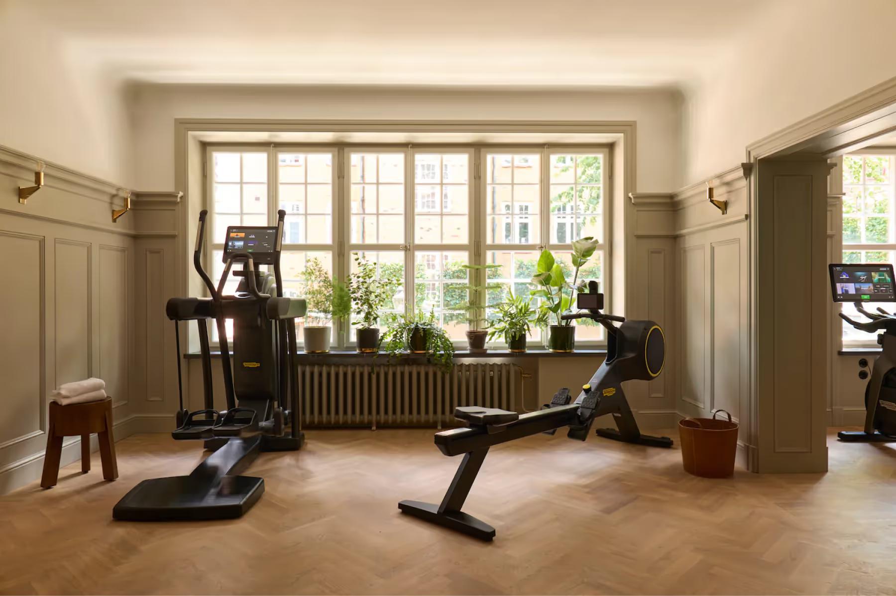 A fitness center with exercise equipment, large windows, and natural light from garden views