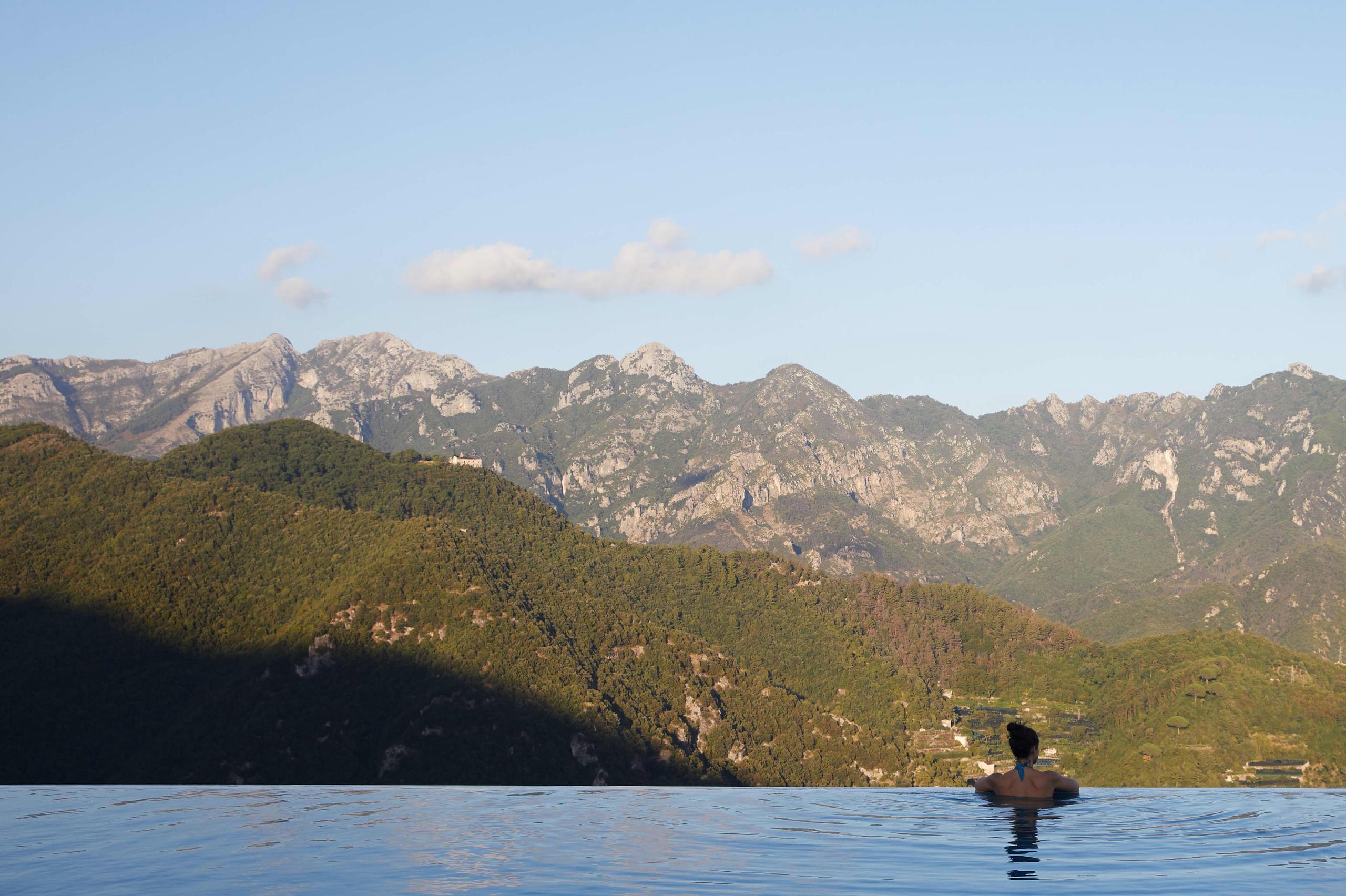 Swimmer in calm turquoise sea with forested mountains and distant coastline landscape