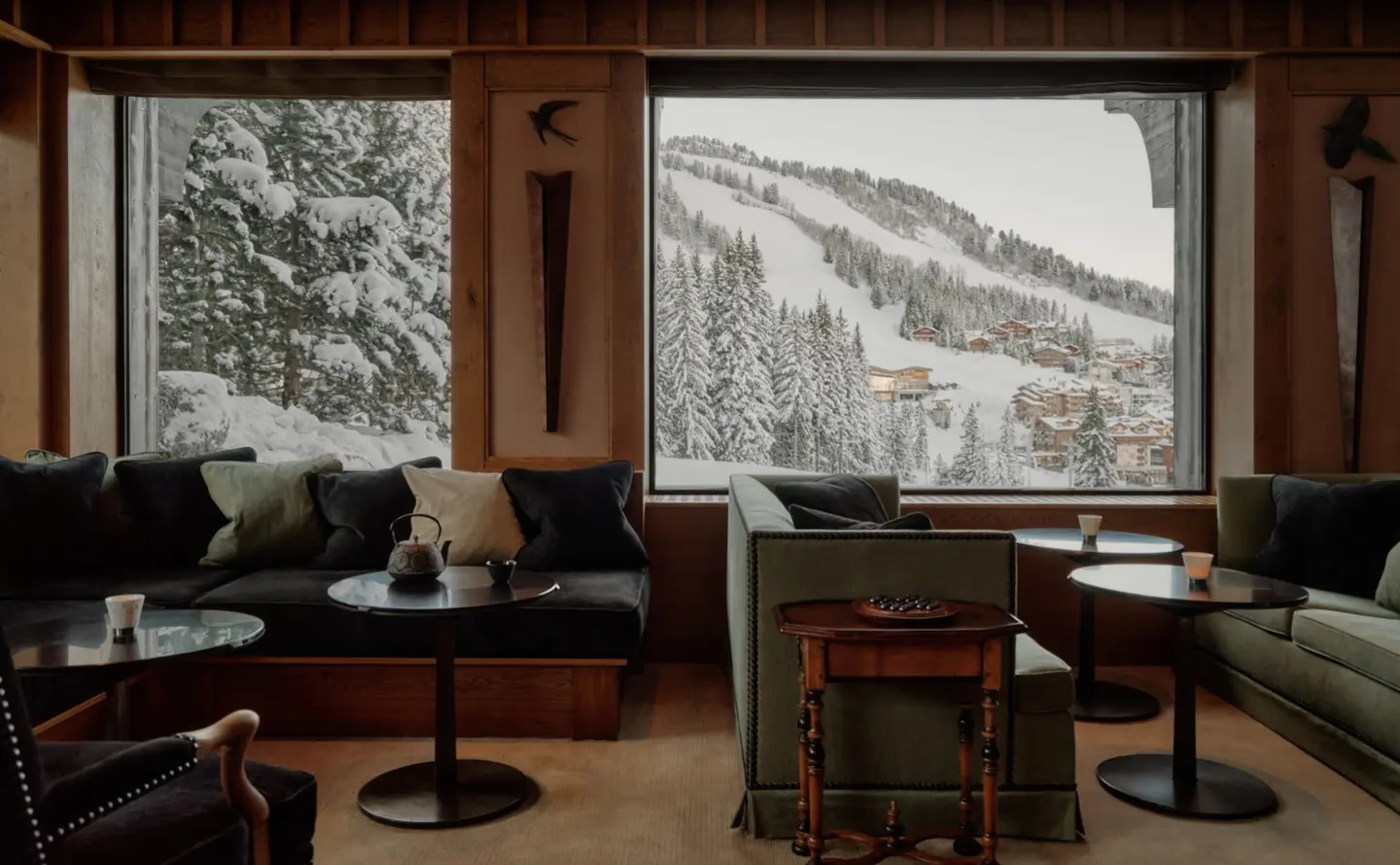 Aman Le Mélézin: lounge with deep green sofas, low round tables, and a teapot set before a mountain view window