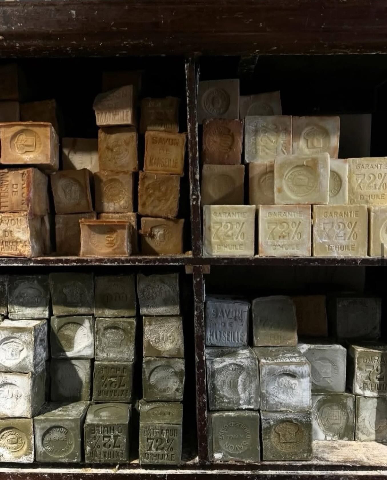 Stacked bars of Marseille soap in different colors on wooden shelves at Maison Empereur in Marseille