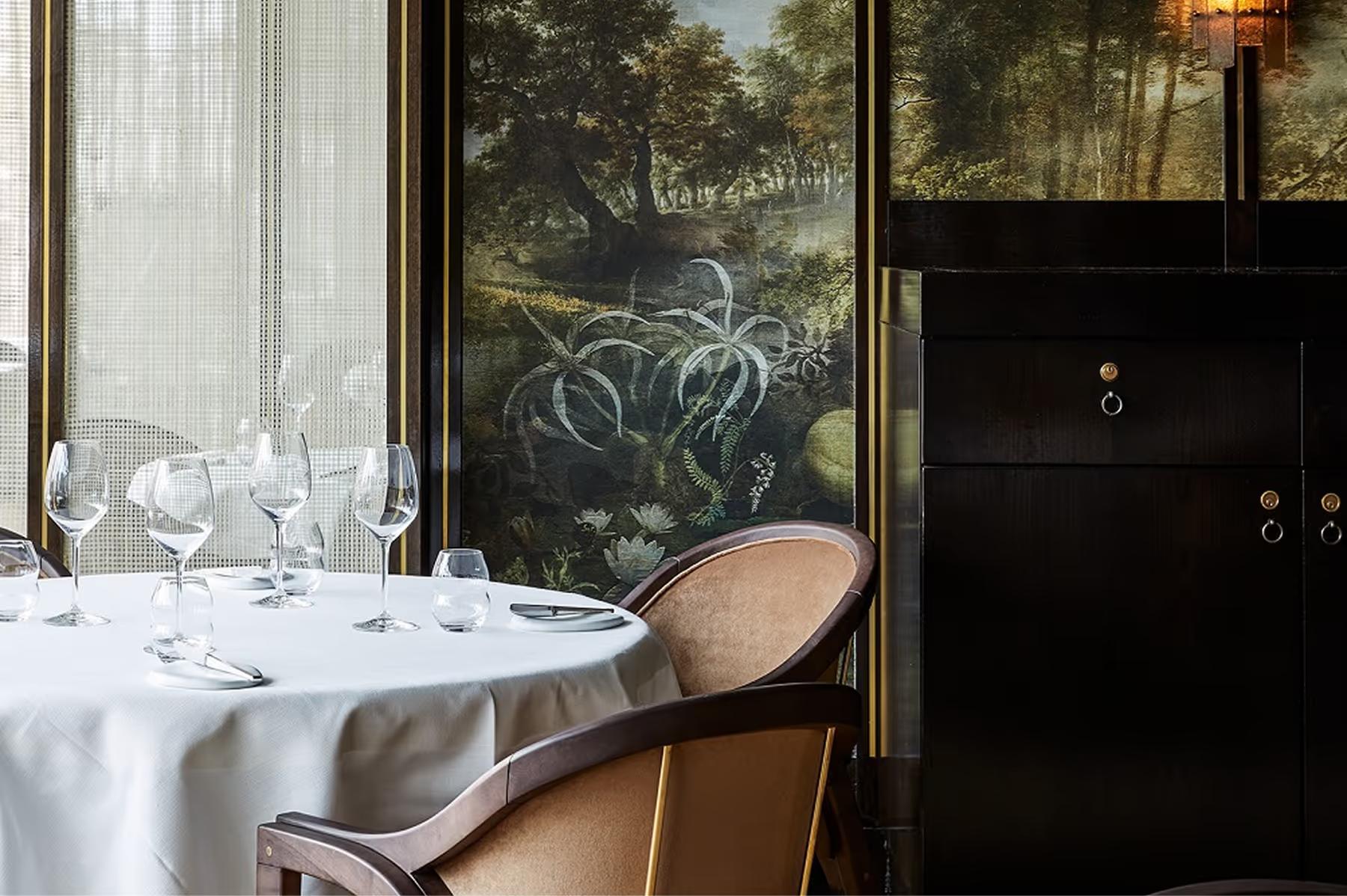 Fine dining room with white tablecloths, large windows overlooking gardens, and formal place settings