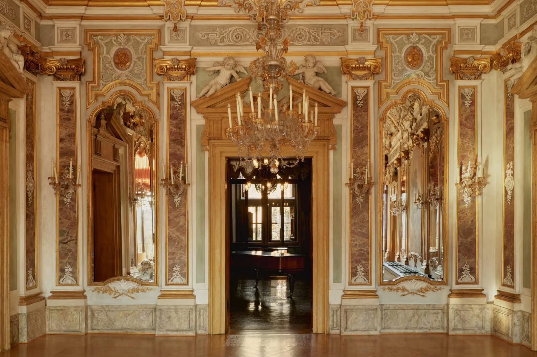 Aman Venice: a neoclassical gallery with cream and gold painted walls, arched alcoves, and ornamental details