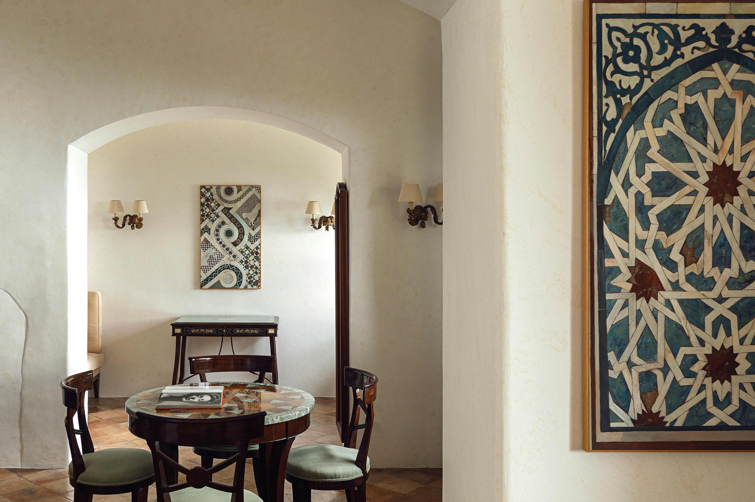 Caruso: gallery space with arched alcove, patterned wall art, round black table, and green upholstered seating