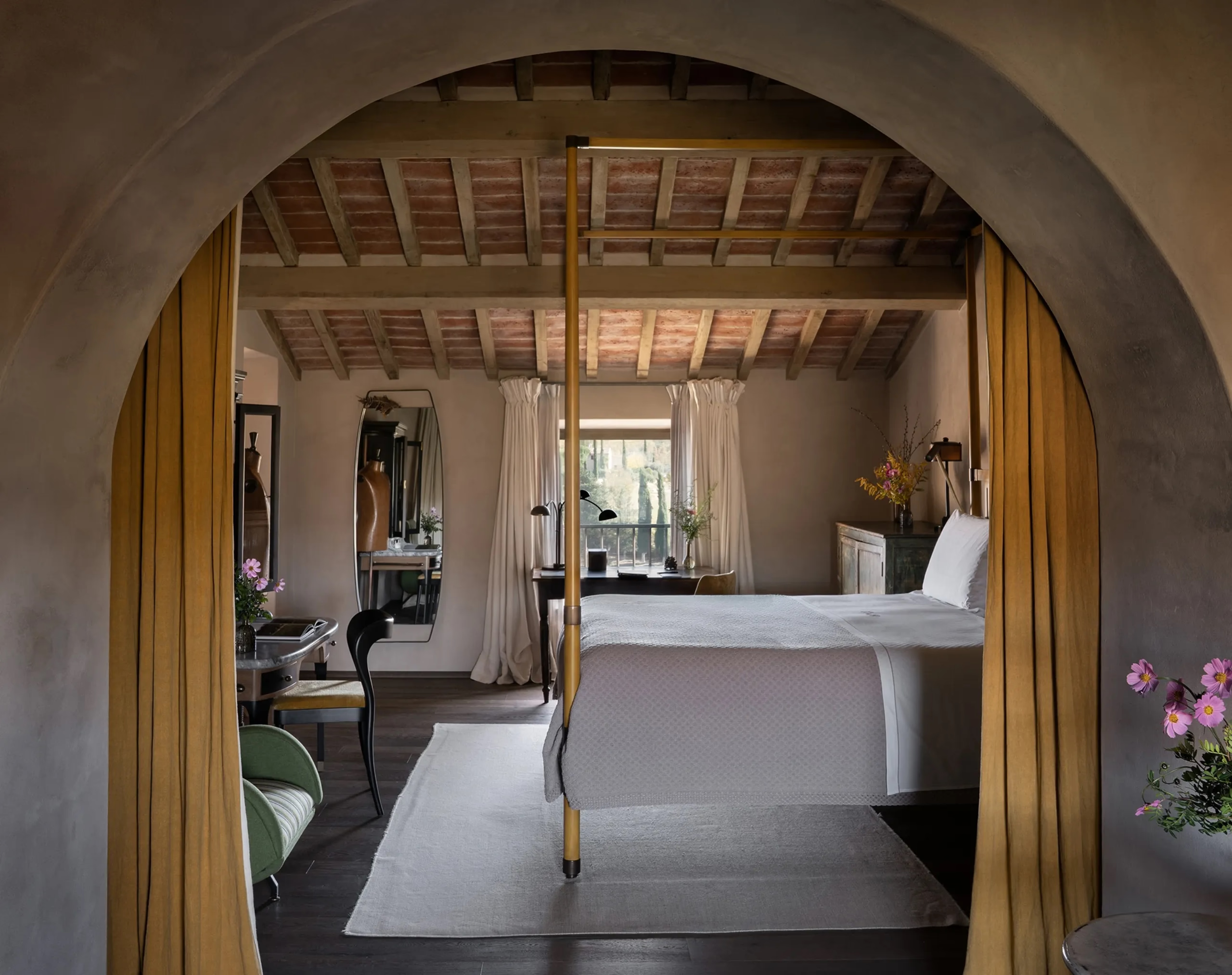 Castello di Reschio: a canopy bed glimpsed through a stone archway, mustard drapes framing the timber beamed bedroom beyond