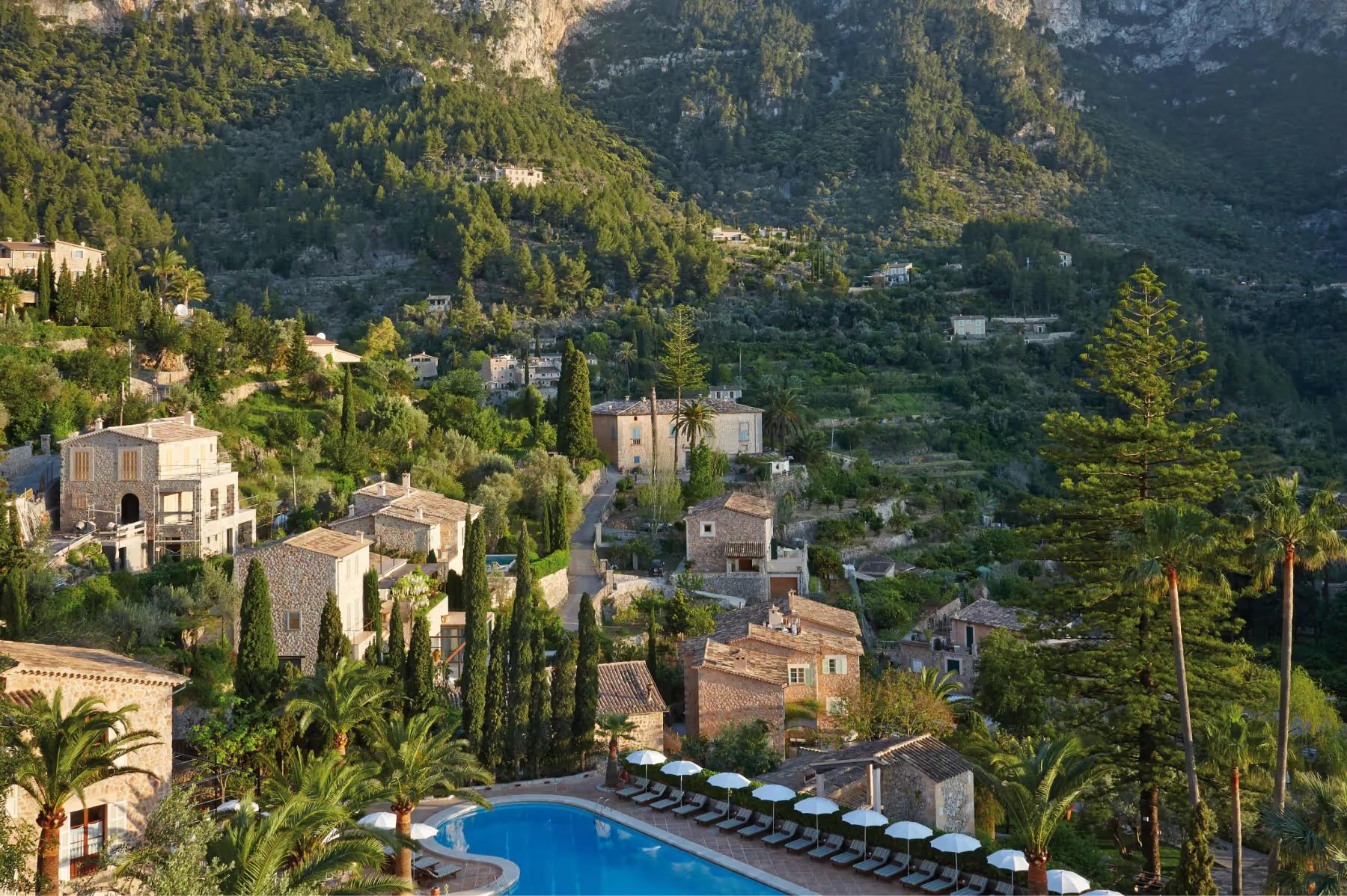 Aerial view of stone buildings cascading down a forested mountainside with turquoise pool