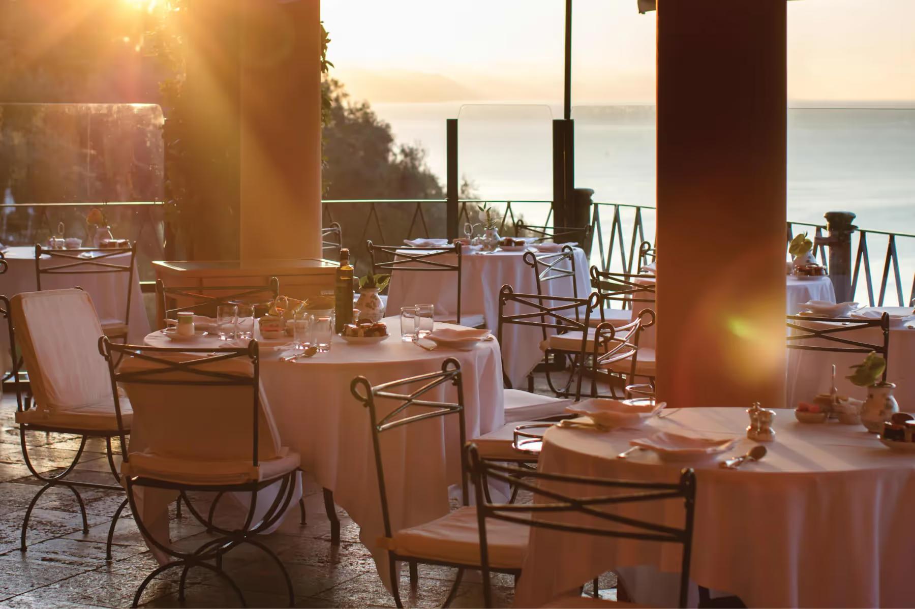 Splendido: an elegant outdoor dining room with table settings and ocean view at sunset