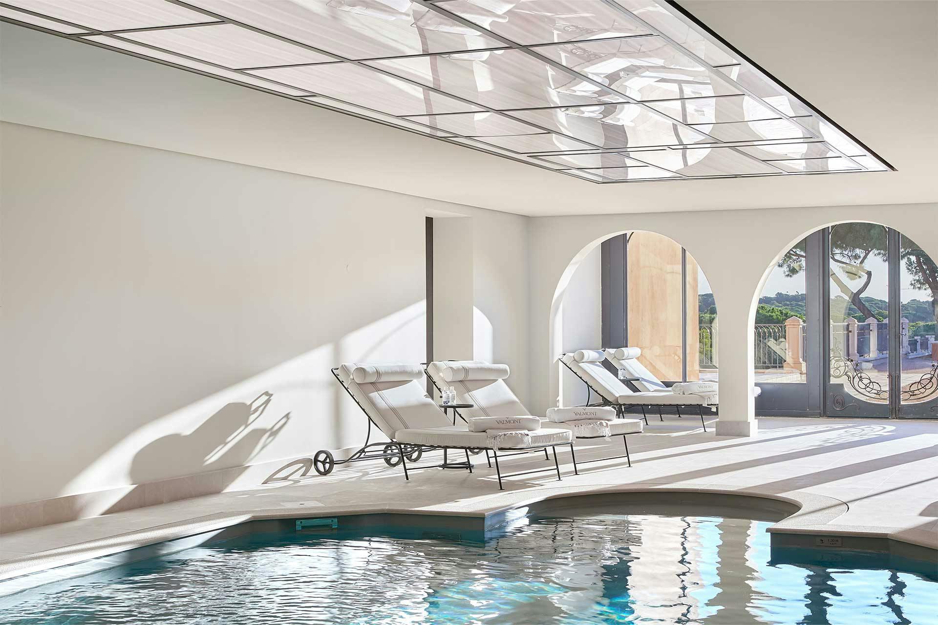 Indoor pool with skylights, white loungers, and bright natural illumination
