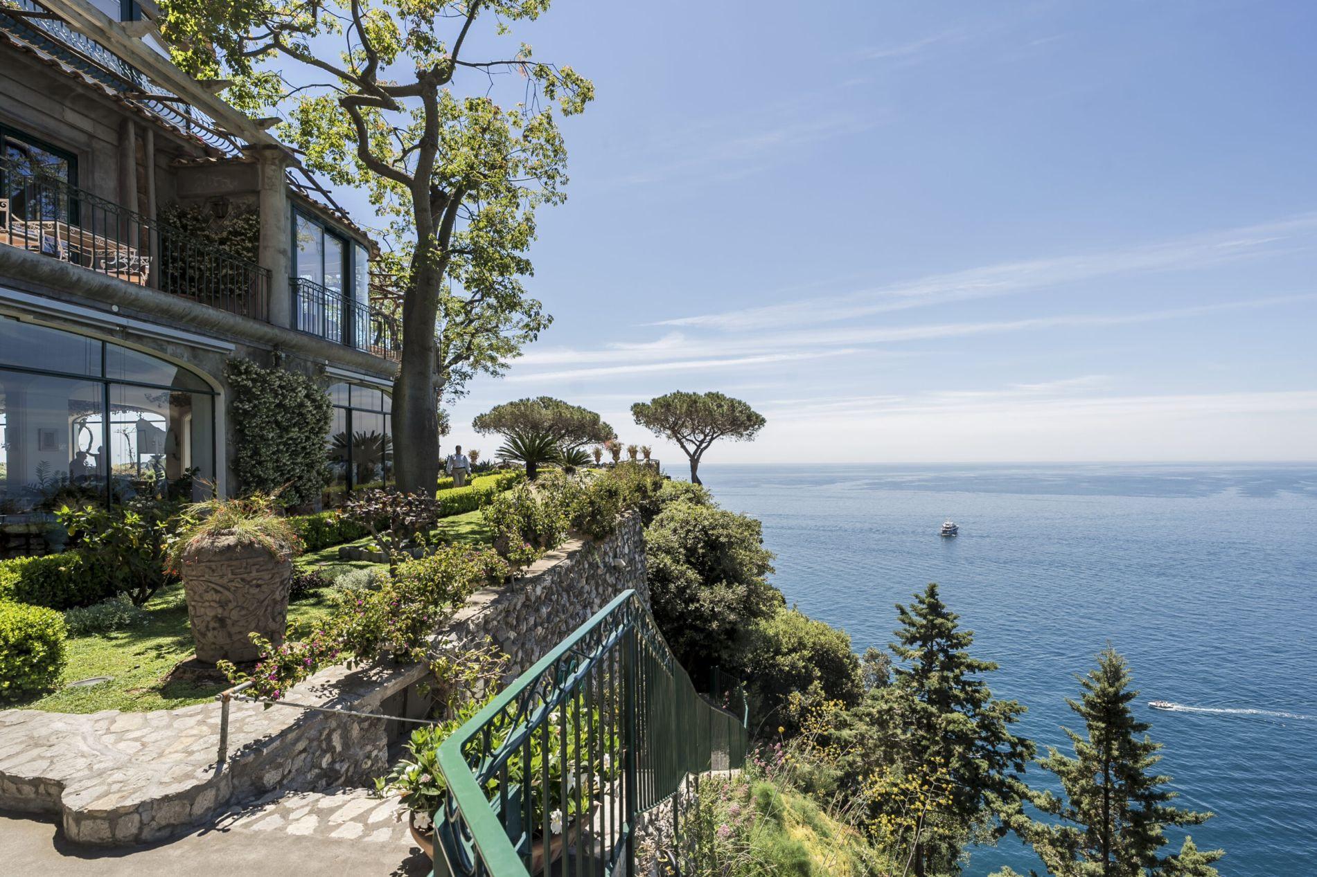 Stone building facade with arched doorways opening to a terrace overlooking blue Mediterranean water