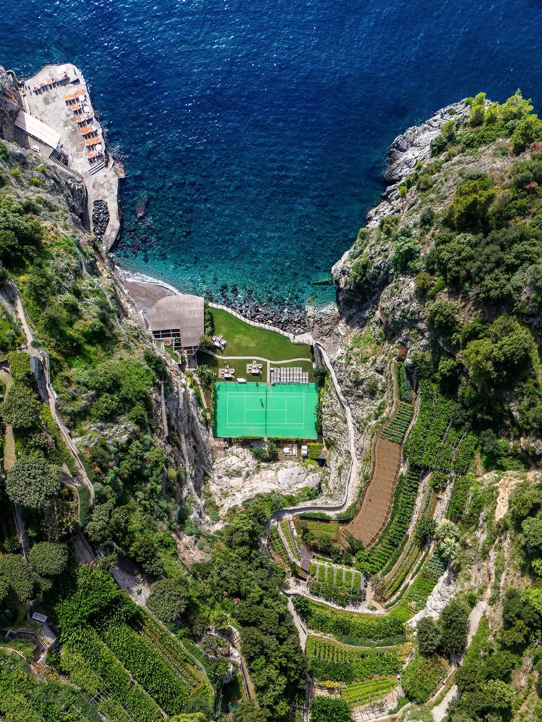 A green tennis court on a terrace cut into the cliff above the sea at Il San Pietro di Positano
