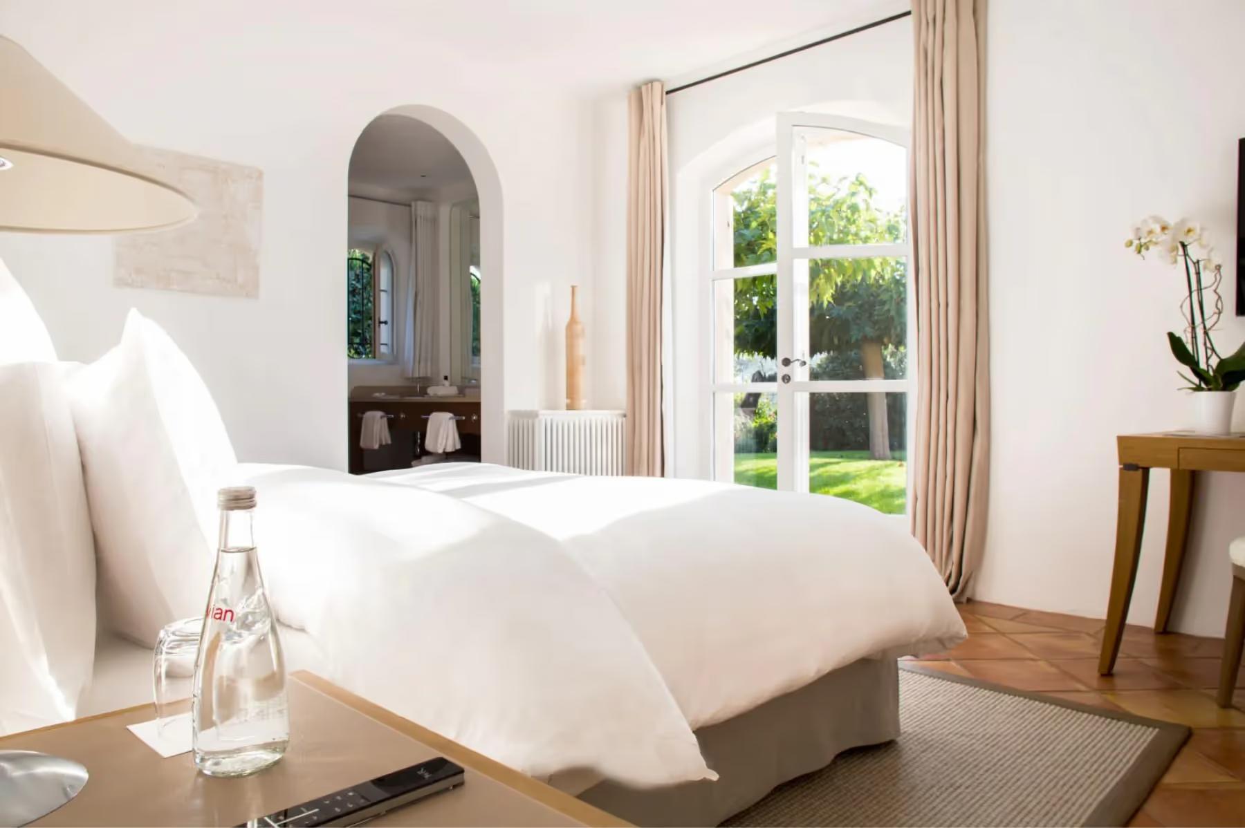 La Réserve Ramatuelle: minimalist white bedroom with arched doorway and garden view