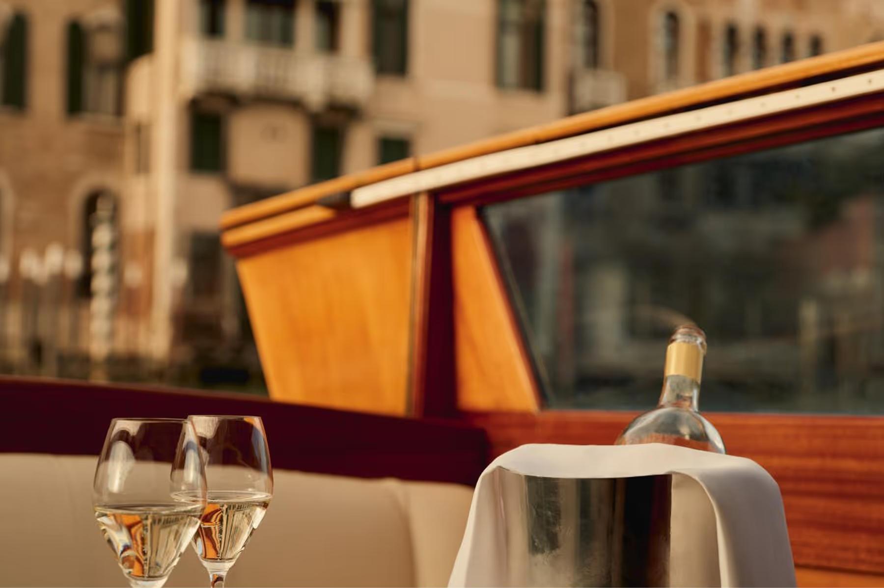Aman Venice: a dining table on a private boat with glasses and the Grand Canal shoreline in the background