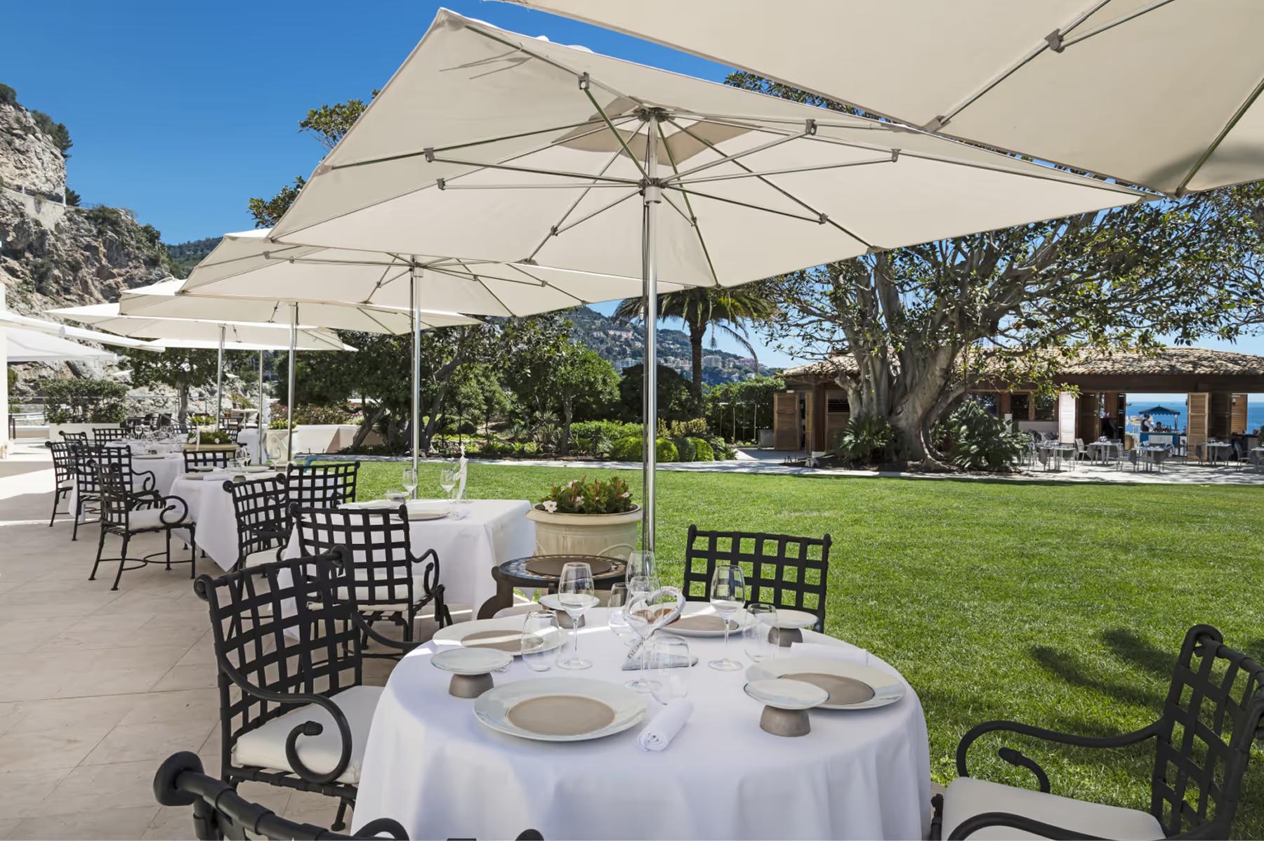 Hotel Cap-Estel: a dining table set with white linens under large umbrellas on a terrace